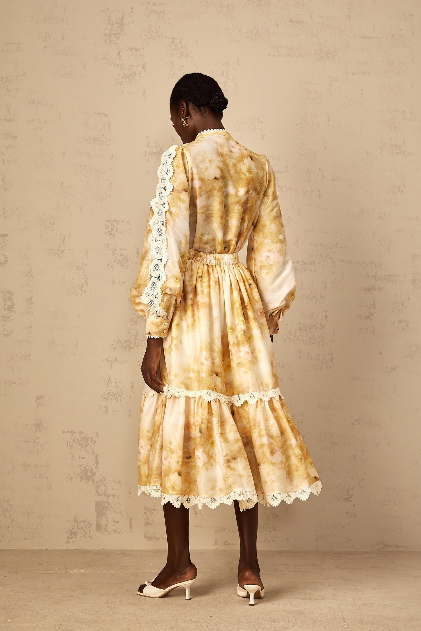 Woman wearing floral print blouse and matching skirt set in light colors standing against plain background