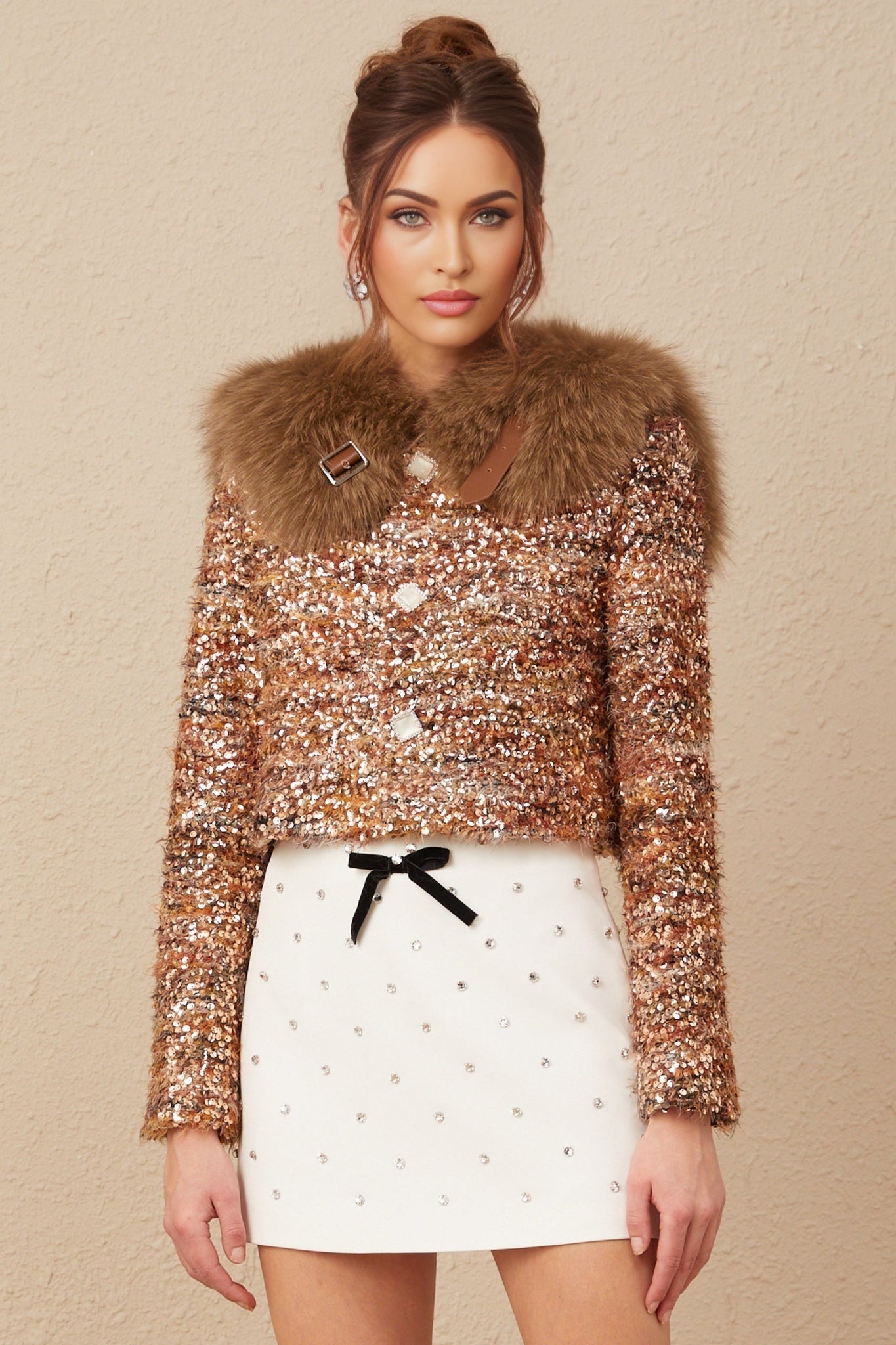 Woman wearing gold sequined jacket with fur trim around collar and cuffs shimmering in light