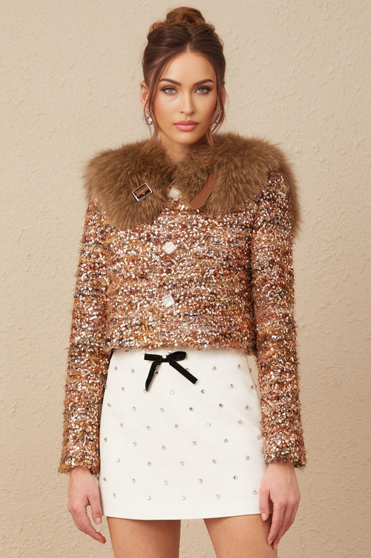 Woman wearing gold sequined jacket with fur trim around collar and cuffs shimmering in light