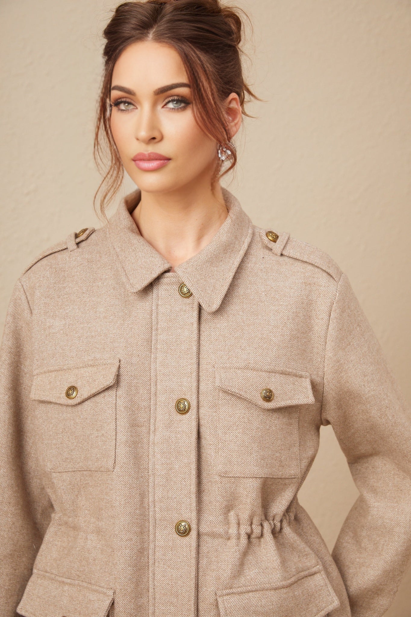 Woman wearing khaki wool twill jacket and matching culottes standing against plain background