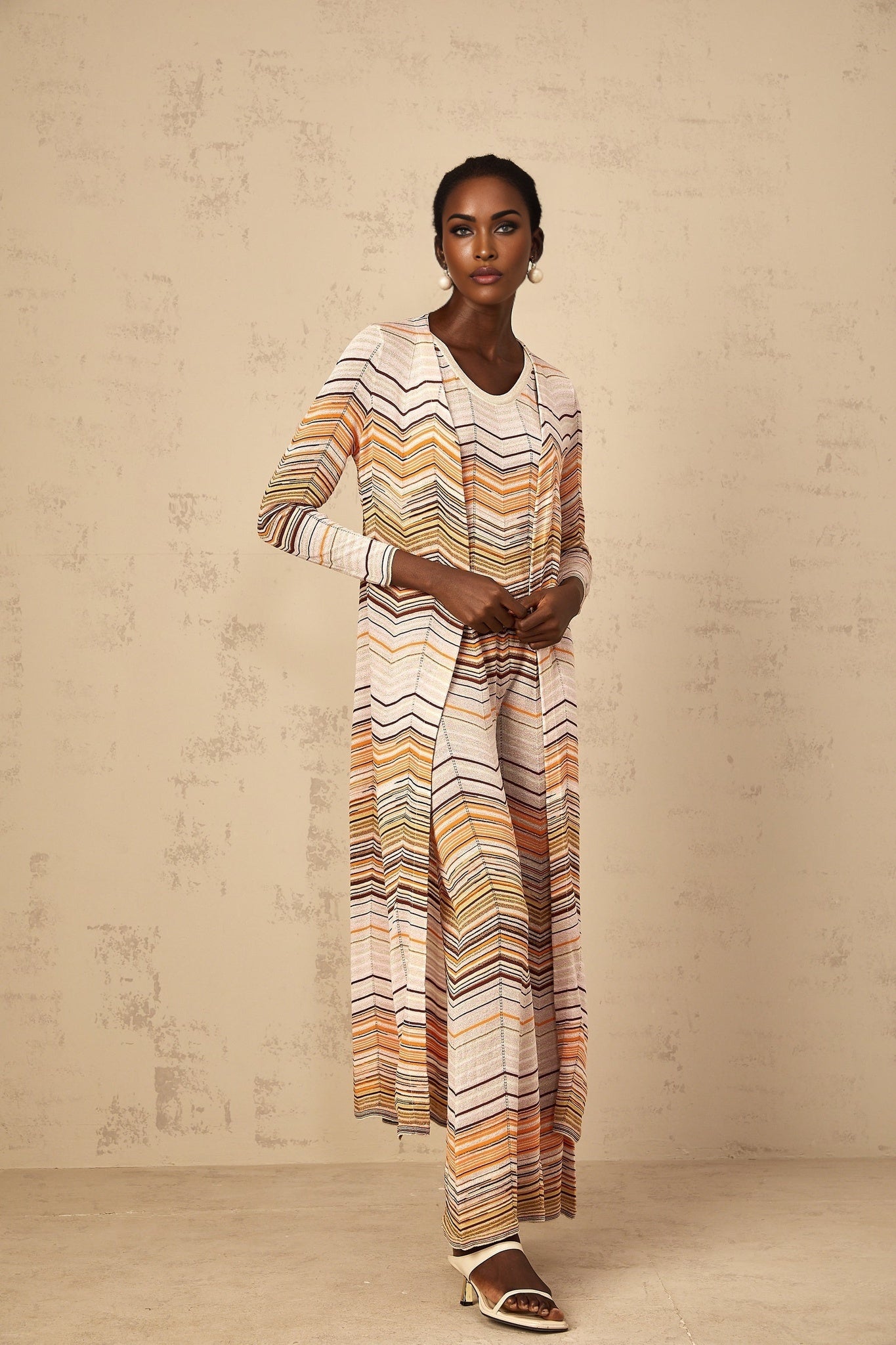 Woman wearing long beige cardigan with horizontal stripes standing against plain background
