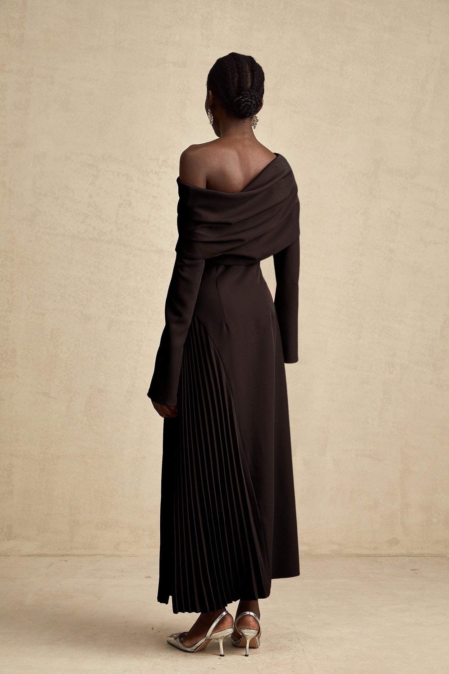 Woman wearing long black pleated maxi dress with high slit posing against plain background