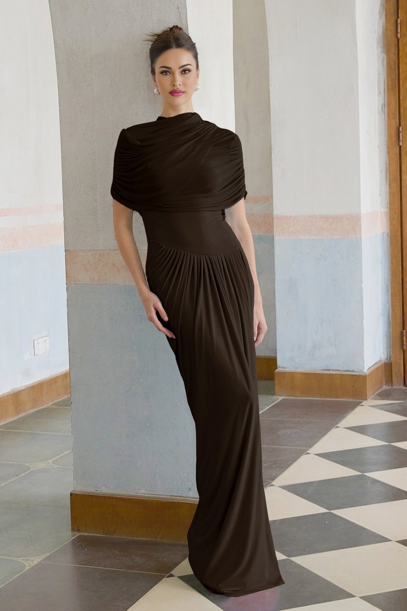 Woman wearing long brown asymmetric pleated maxi dress with flowing skirt and one shoulder design