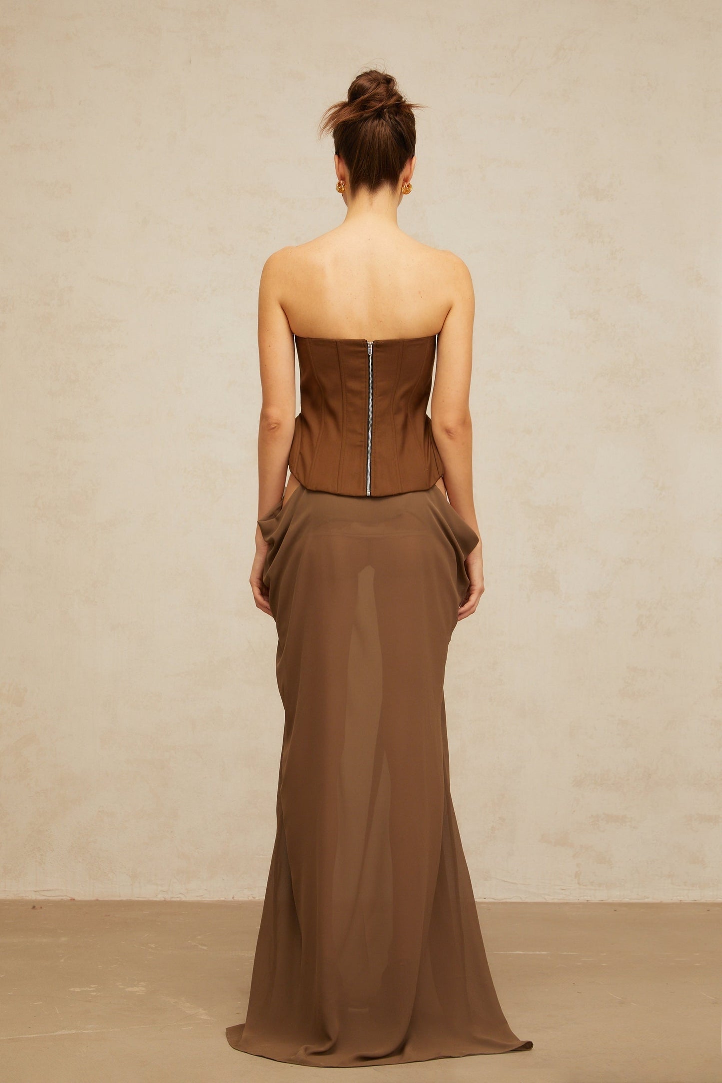 Woman wearing long brown corset maxi dress with butterfly pin detail and flowy skirt