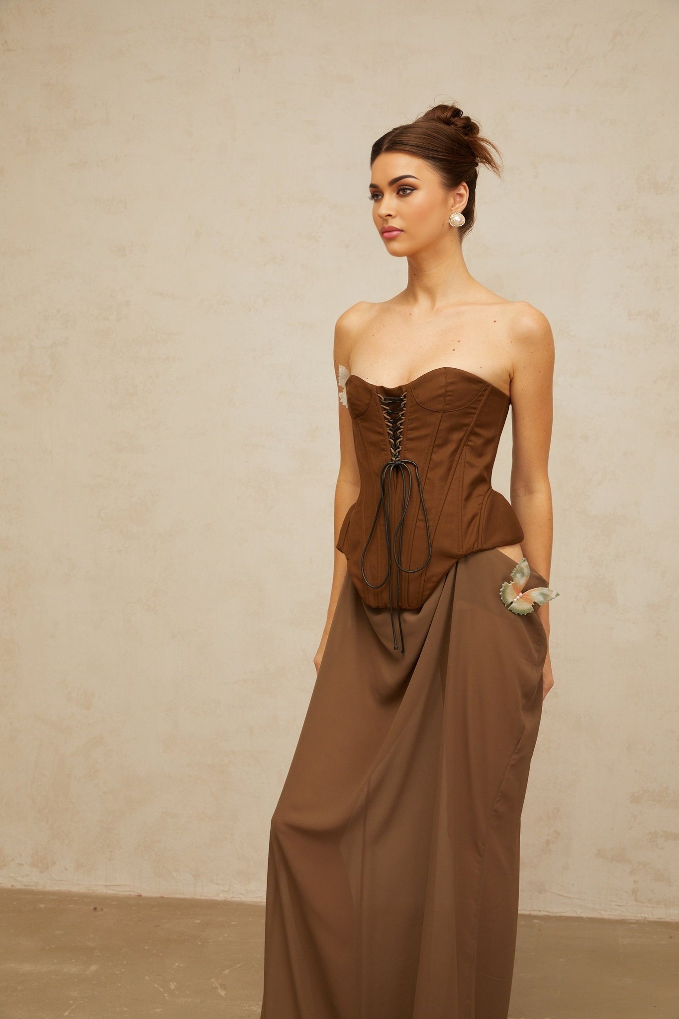 Woman wearing long brown maxi dress with corset bodice and butterfly pin detail