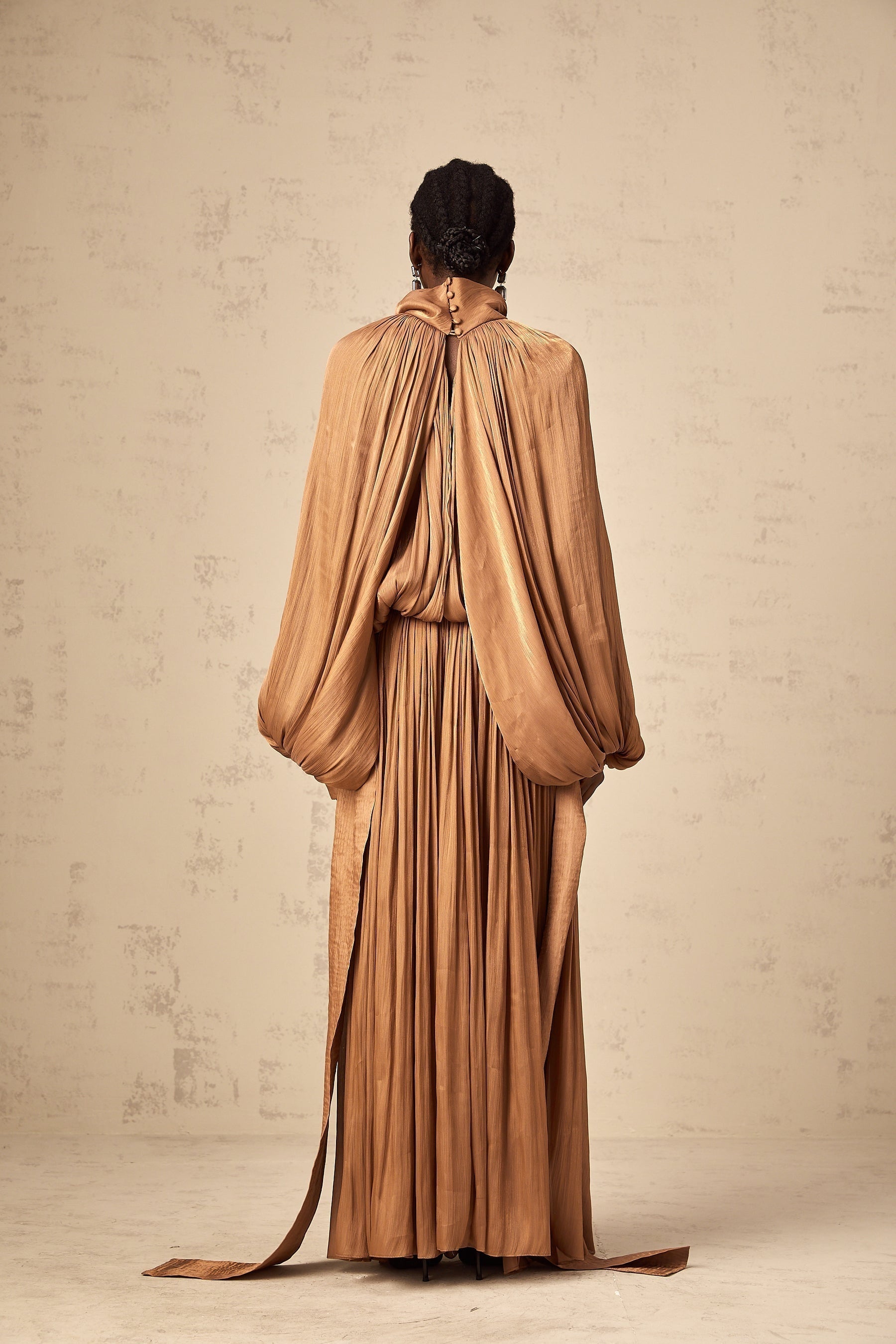 Woman wearing long brown pleated satin maxi dress with flowing skirt and fitted bodice