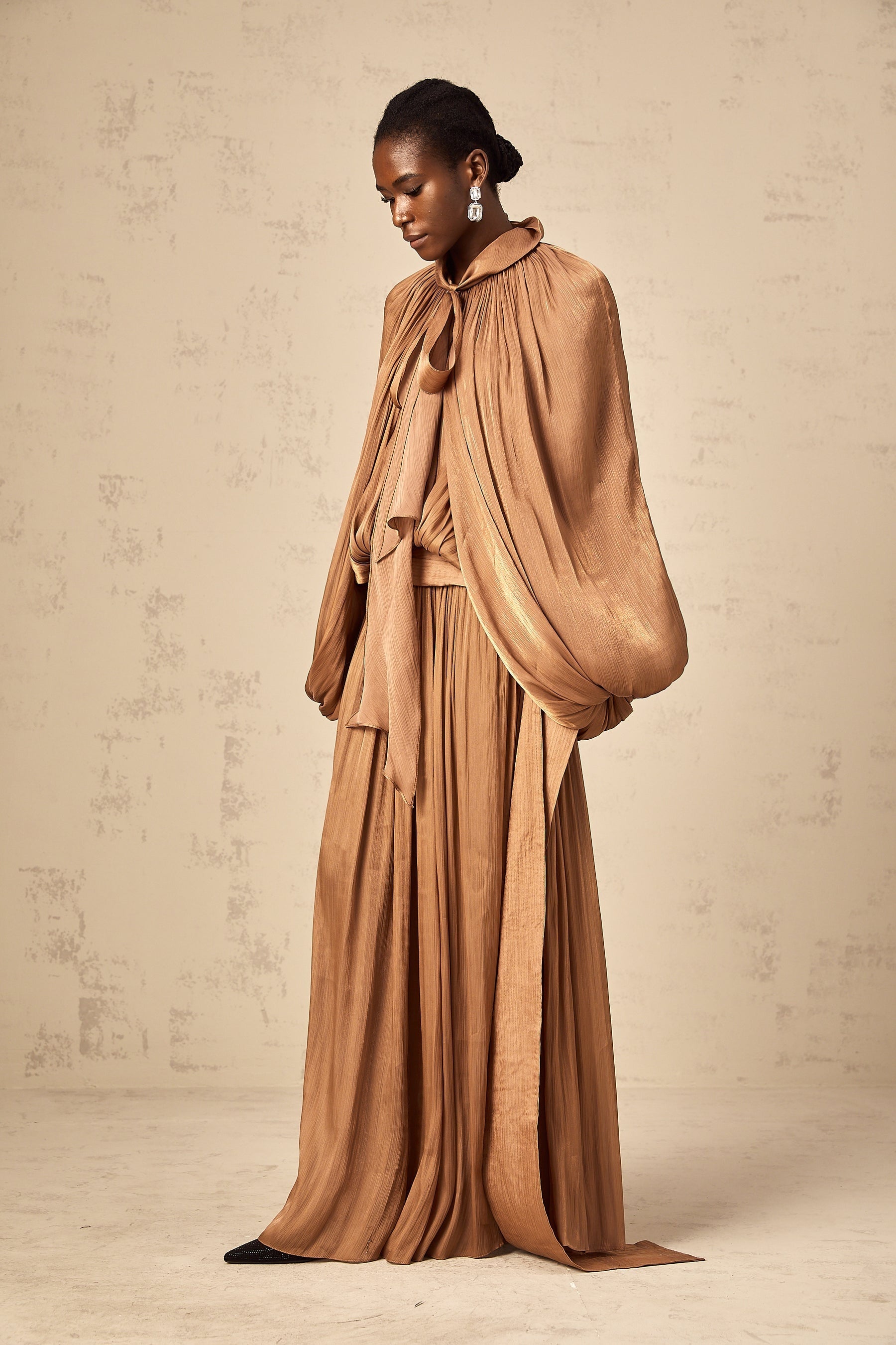 Woman wearing long brown pleated satin maxi dress with flowing skirt and fitted bodice