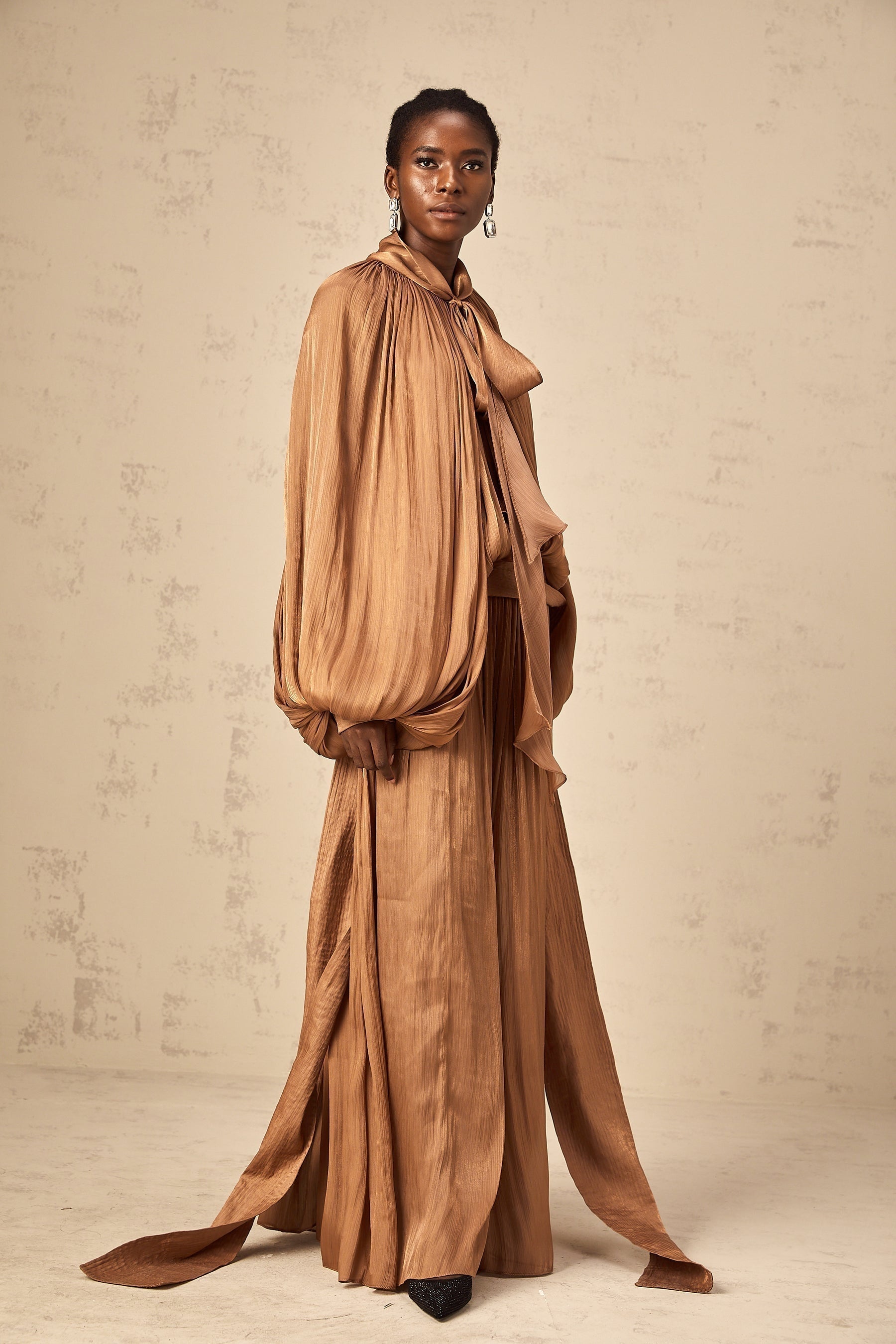 Woman wearing long brown pleated satin maxi dress with flowing skirt and fitted bodice
