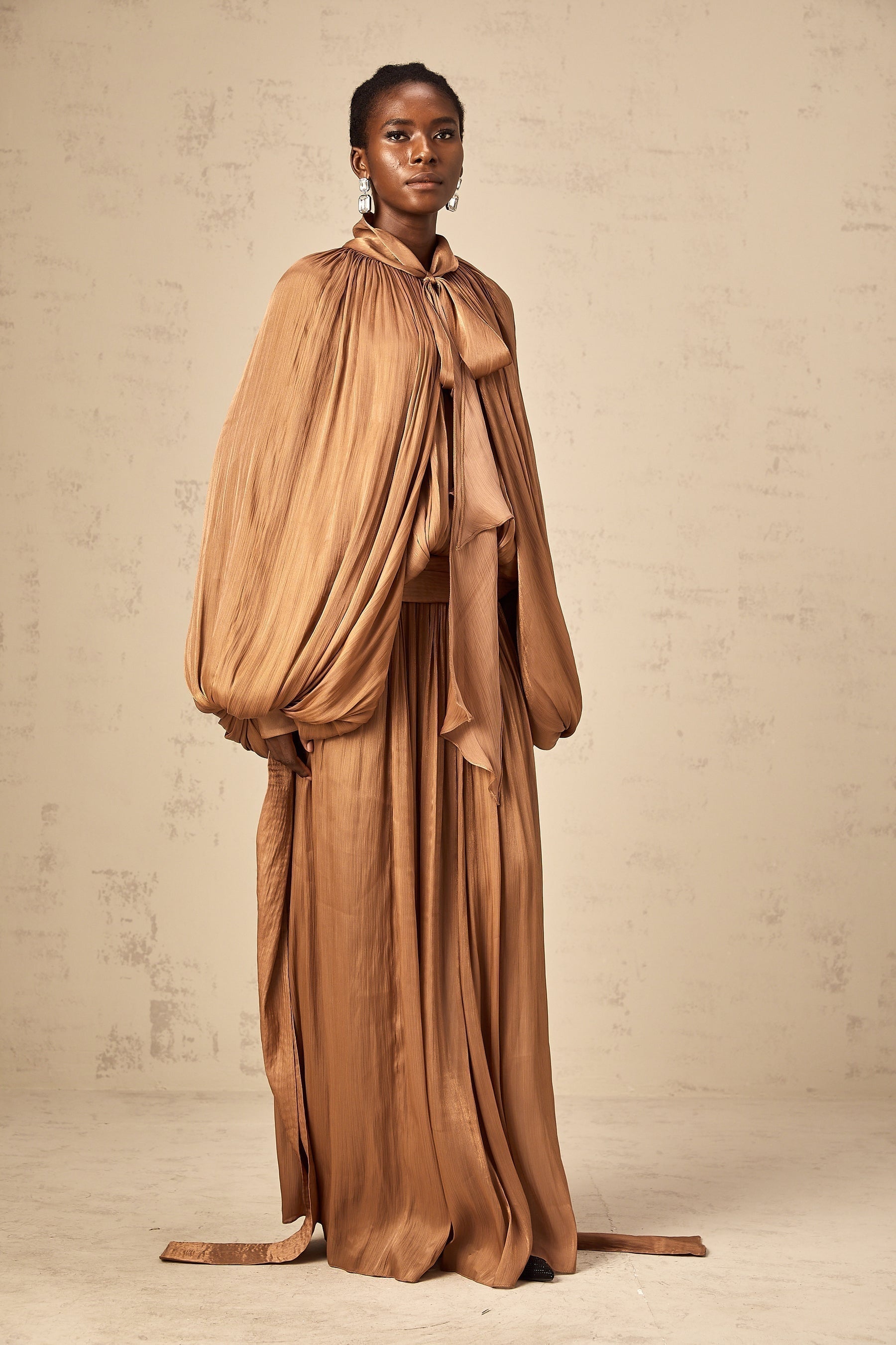 Woman wearing long brown pleated satin maxi dress with flowy skirt and fitted bodice