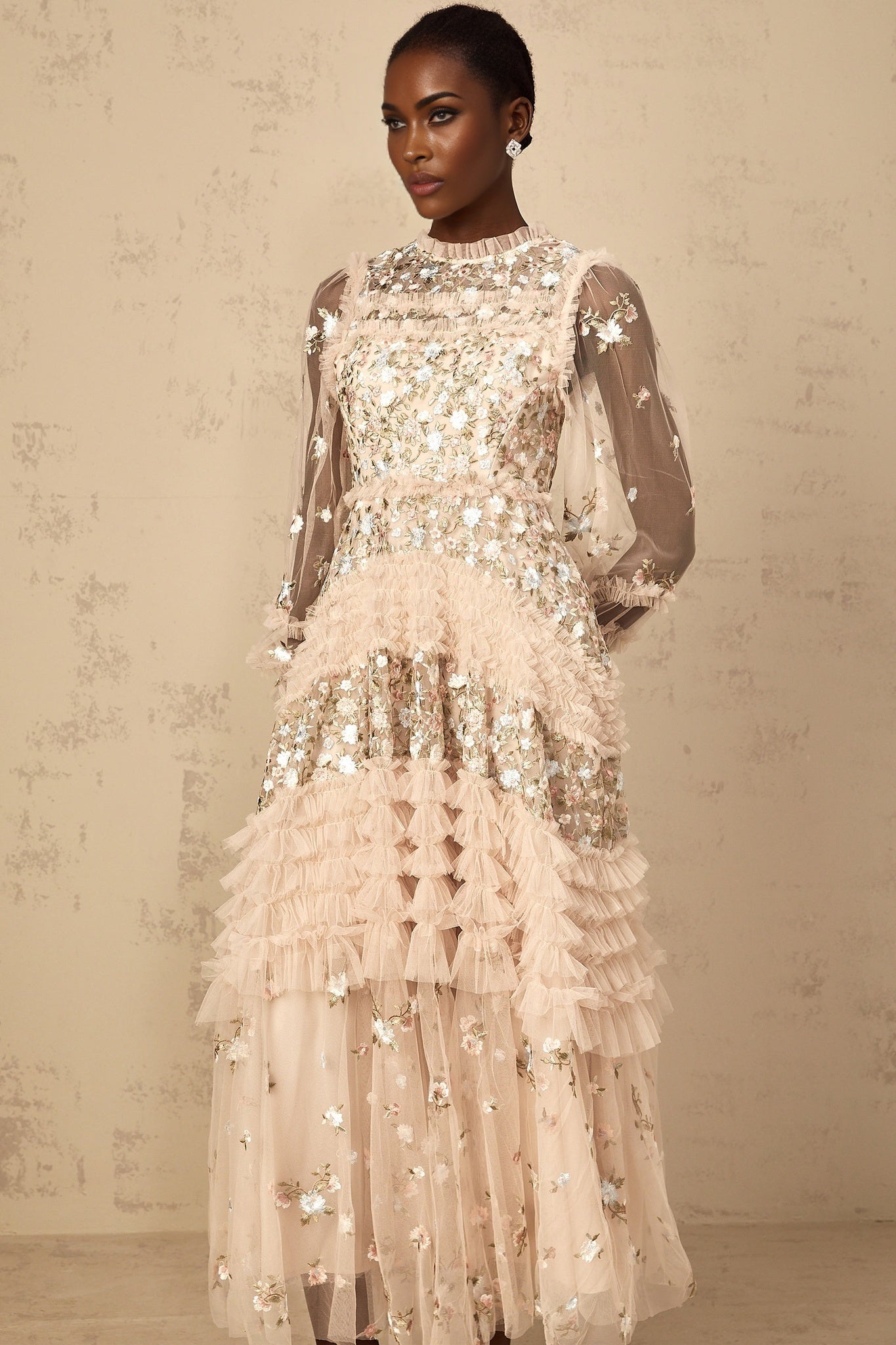 Woman wearing long flowy tulle maxi dress with floral embroidery and tiered skirt design