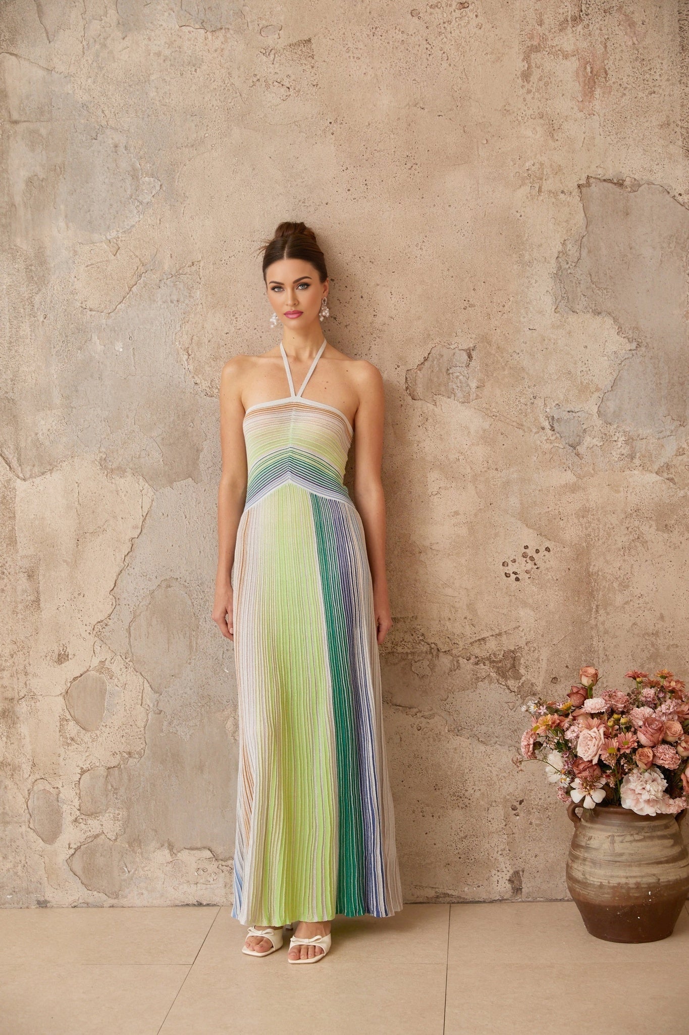 Woman wearing long metallic knit maxi dress with backless design standing in elegant pose