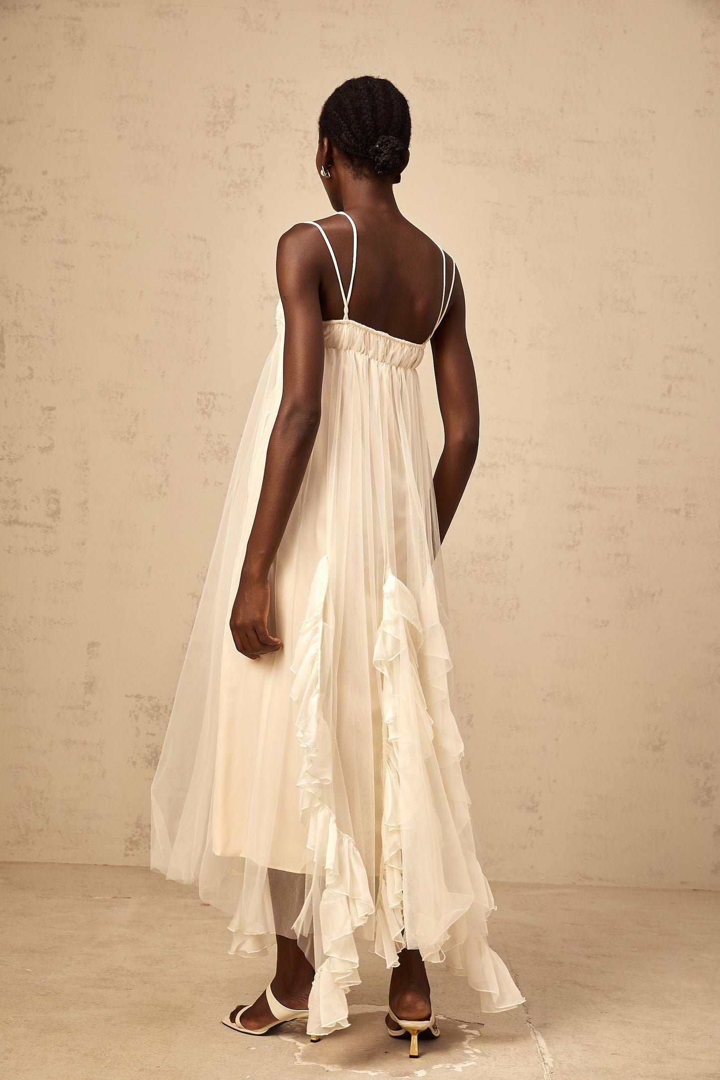 Woman wearing long neutral colored maxi dress with layered ruffled tulle skirt and fitted bodice