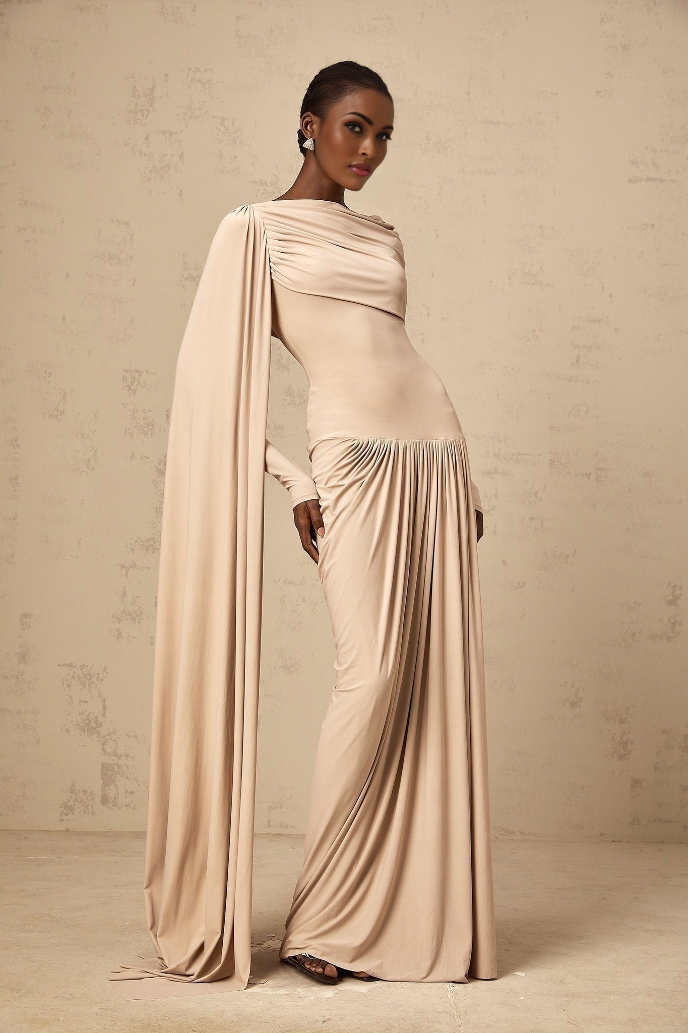 Woman wearing long neutral colored maxi dress with ribbon design details and draped fabric