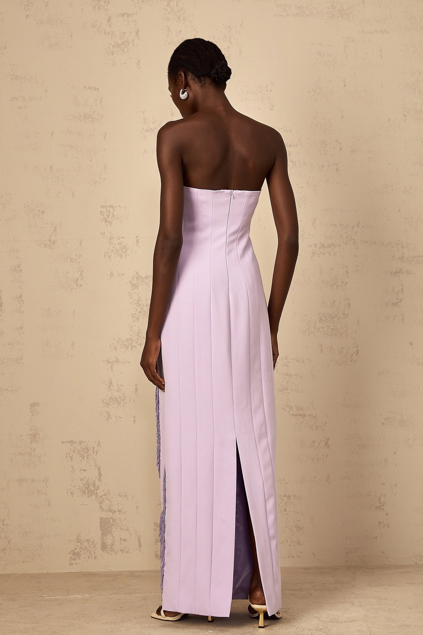 Woman wearing long purple maxi dress with beaded fringe details and spaghetti straps standing against plain background