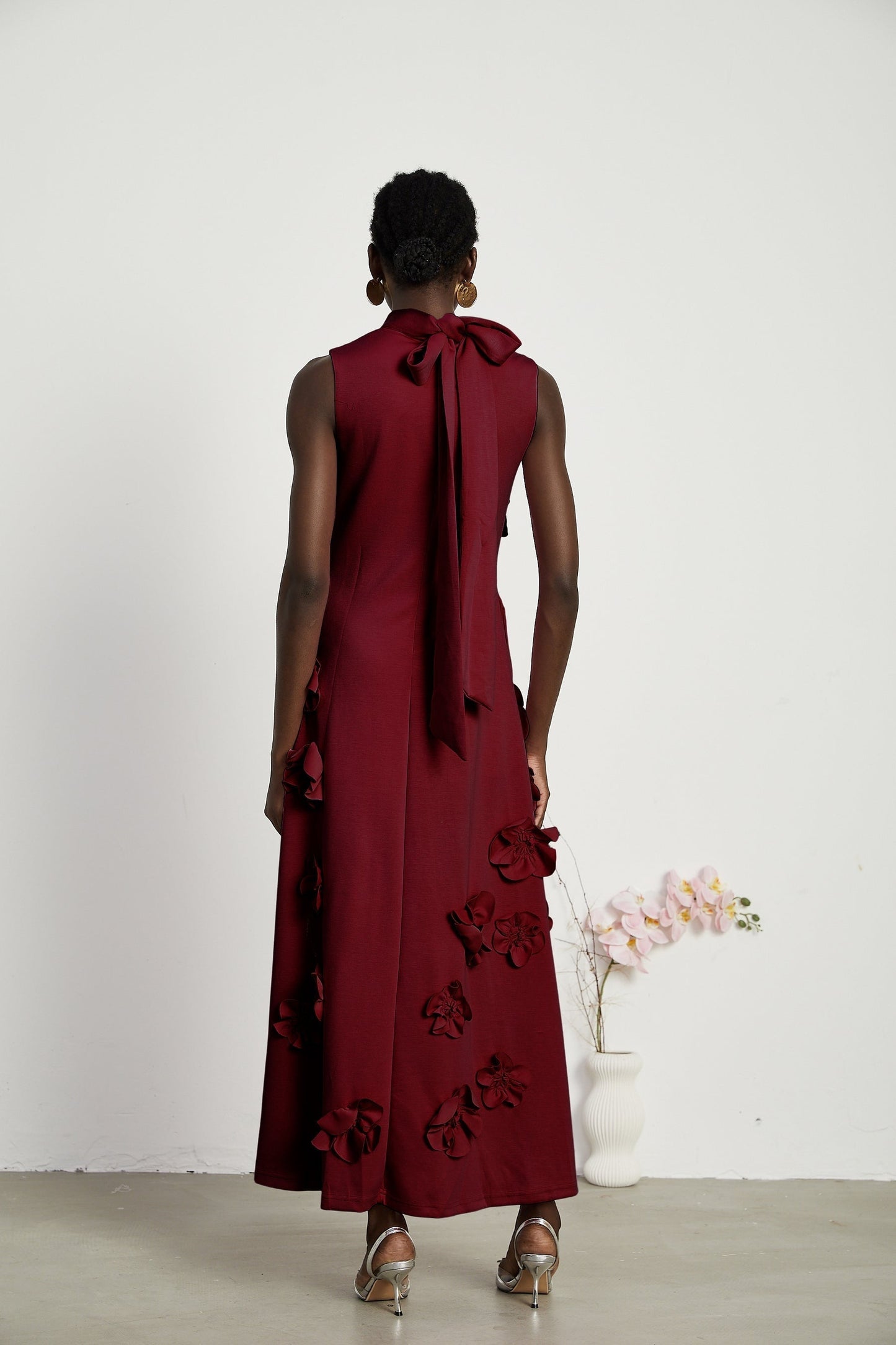 Woman wearing long red sleeveless maxi dress with bow tie detail and faux flower embellishments
