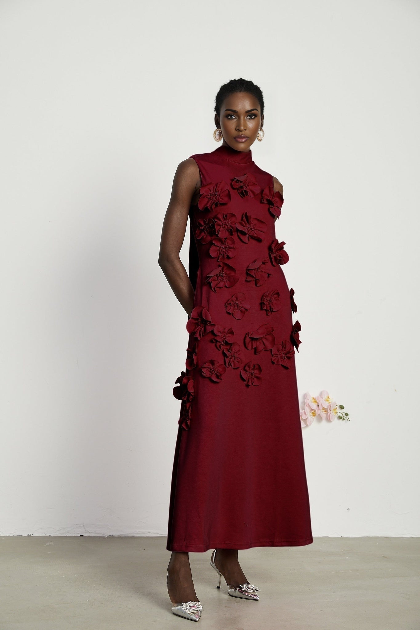 Woman wearing long red sleeveless maxi dress with bow tie detail and faux flower embellishments