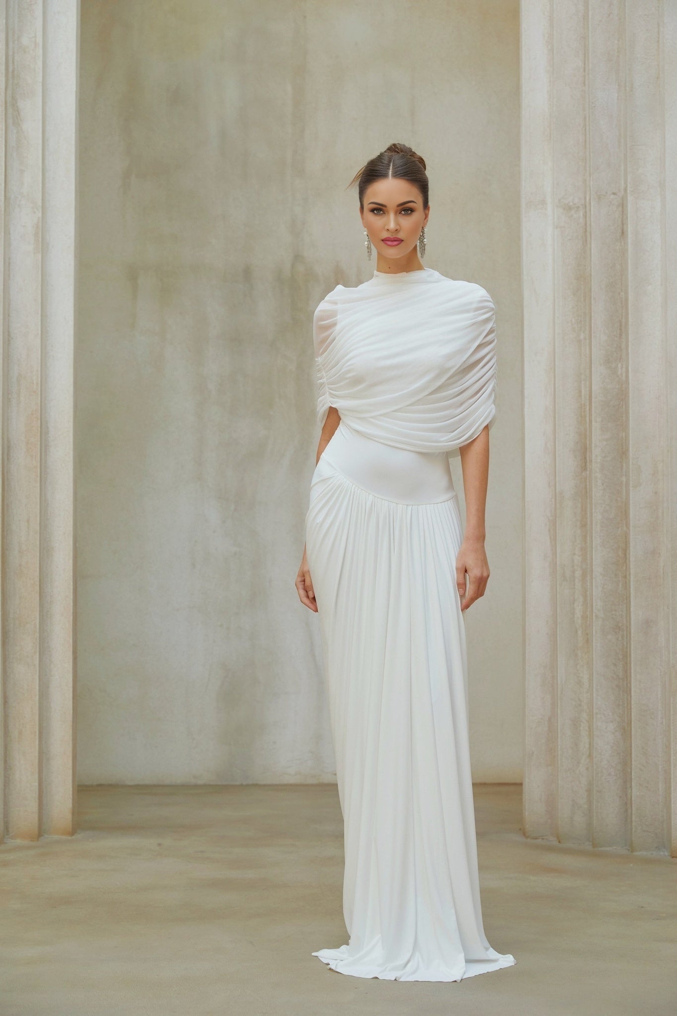 Woman wearing long white asymmetrical pleated maxi dress with flowing skirt and sleeveless design