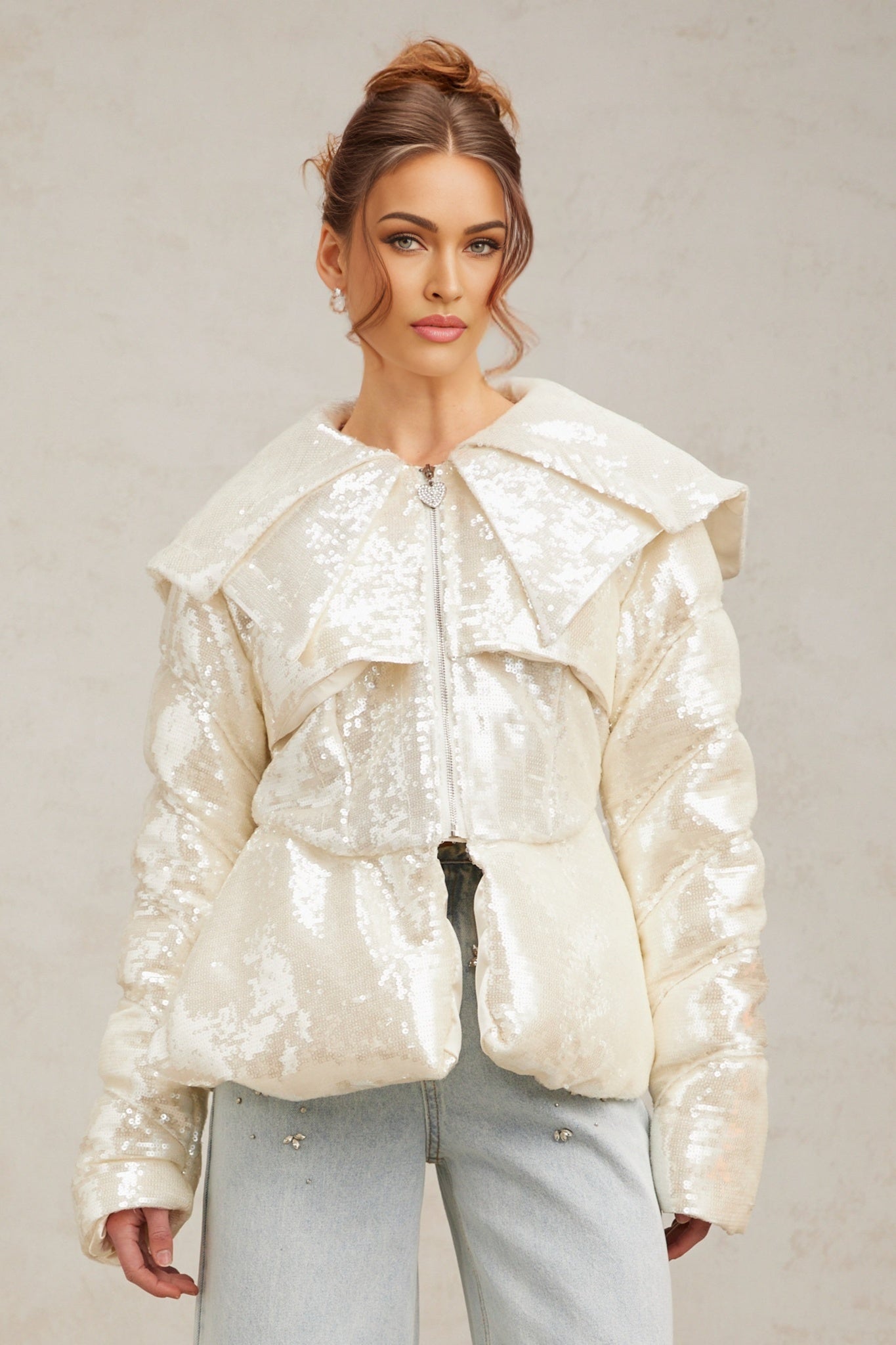 Woman wearing long white down coat with sequin details standing against plain background