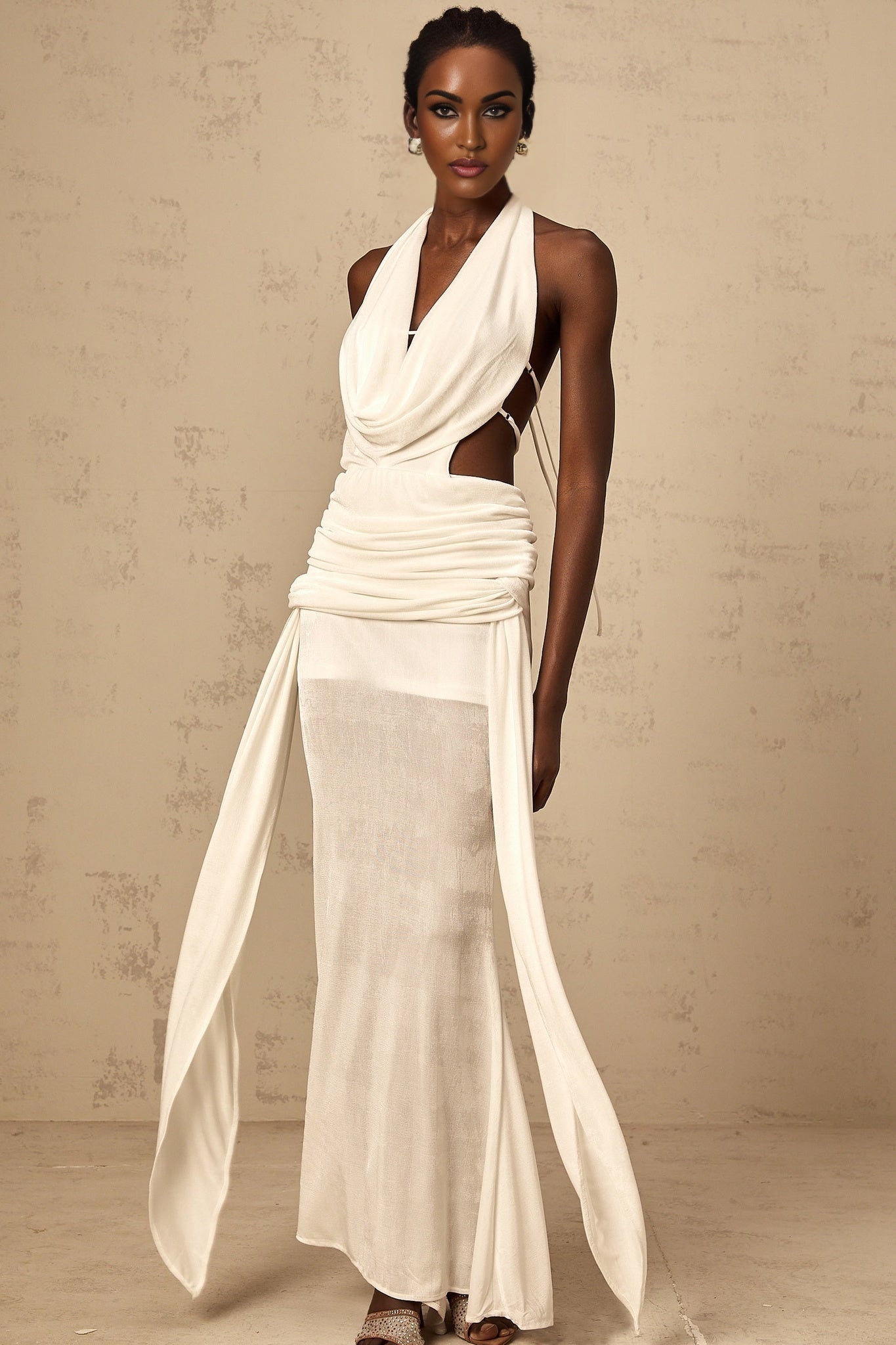 Woman wearing long white halterneck maxi dress with open back standing in sunlit outdoor setting
