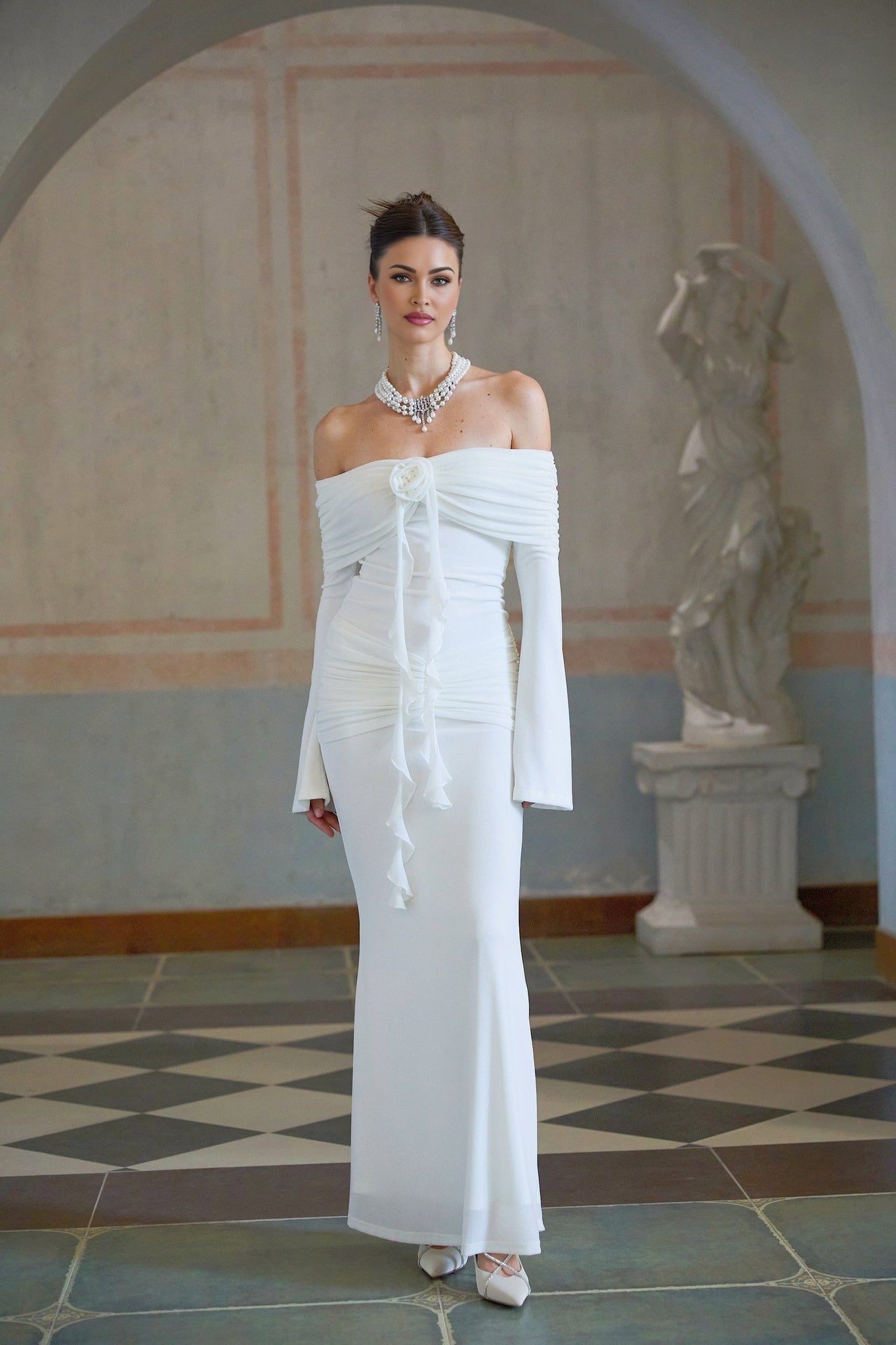 Woman wearing long white knit maxi dress with glittery floral appliques standing in neutral background