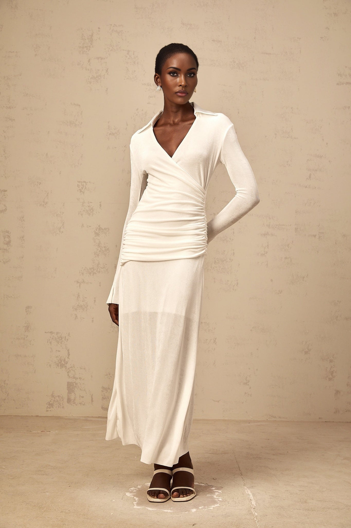 Woman wearing long white knitted maxi dress with ruched detailing and fitted silhouette