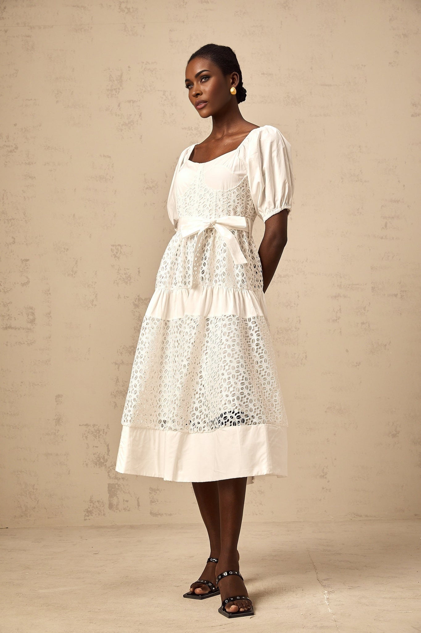 Woman wearing long white lace dress with tiered skirt and corded lace details standing in elegant pose