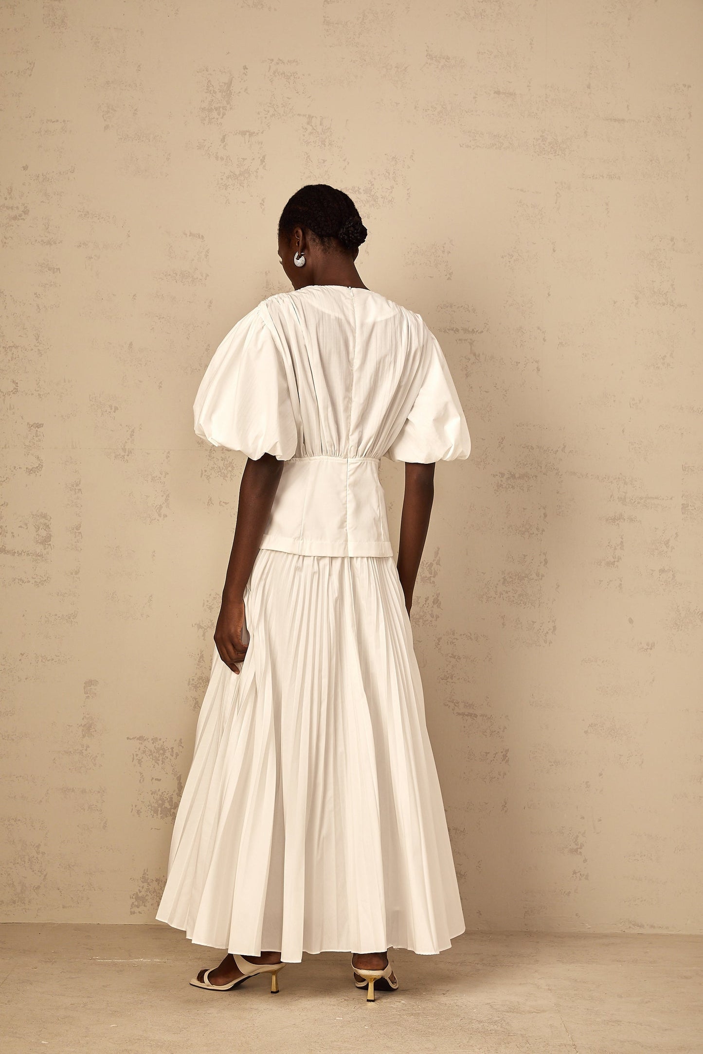Woman wearing long white pleated maxi dress with laceup detail