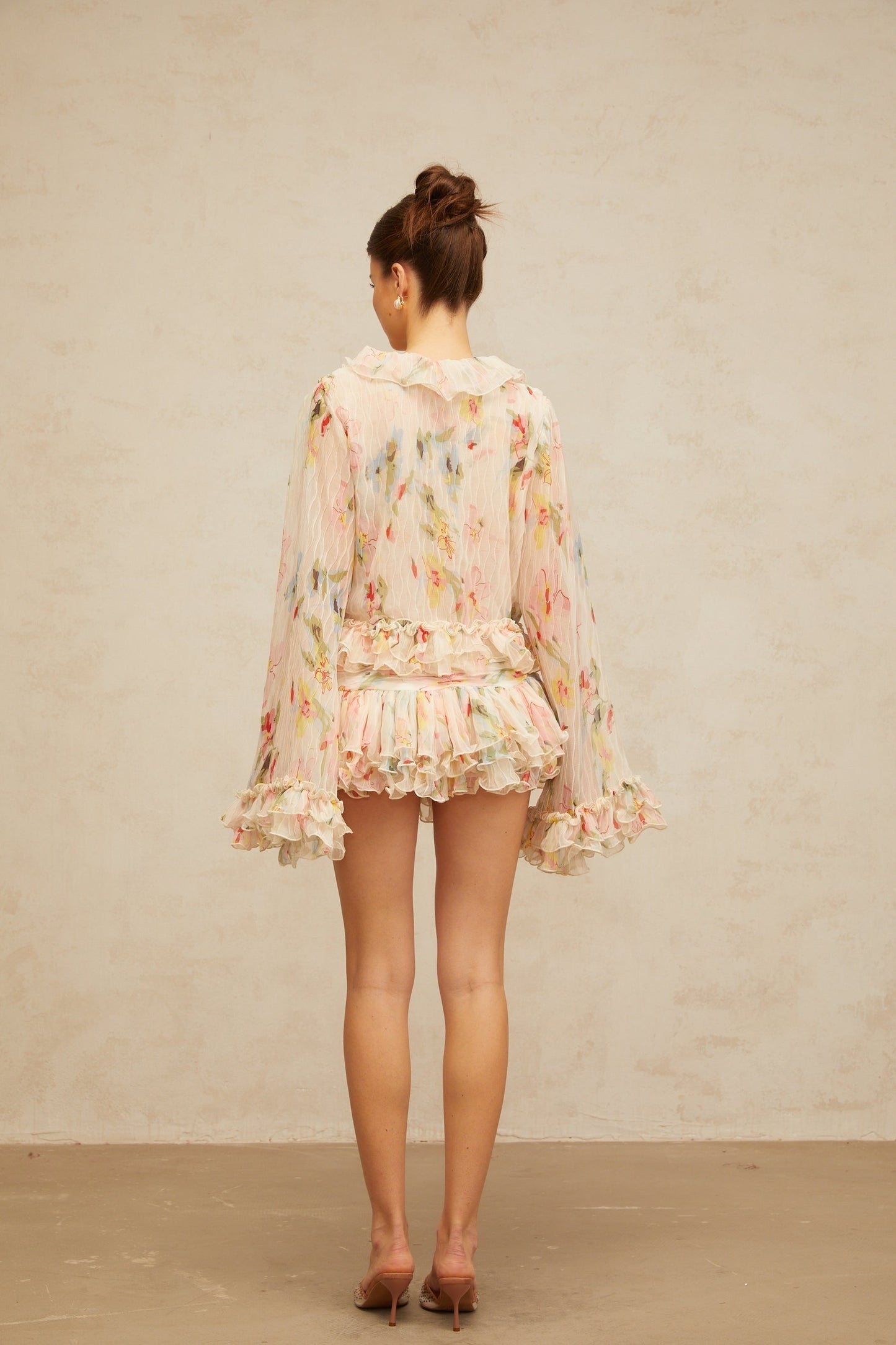 Woman wearing matching floral print blouse and skirt set Blouse has ruffled details Skirt falls below knee Both pieces feature colorful floral pattern on light background