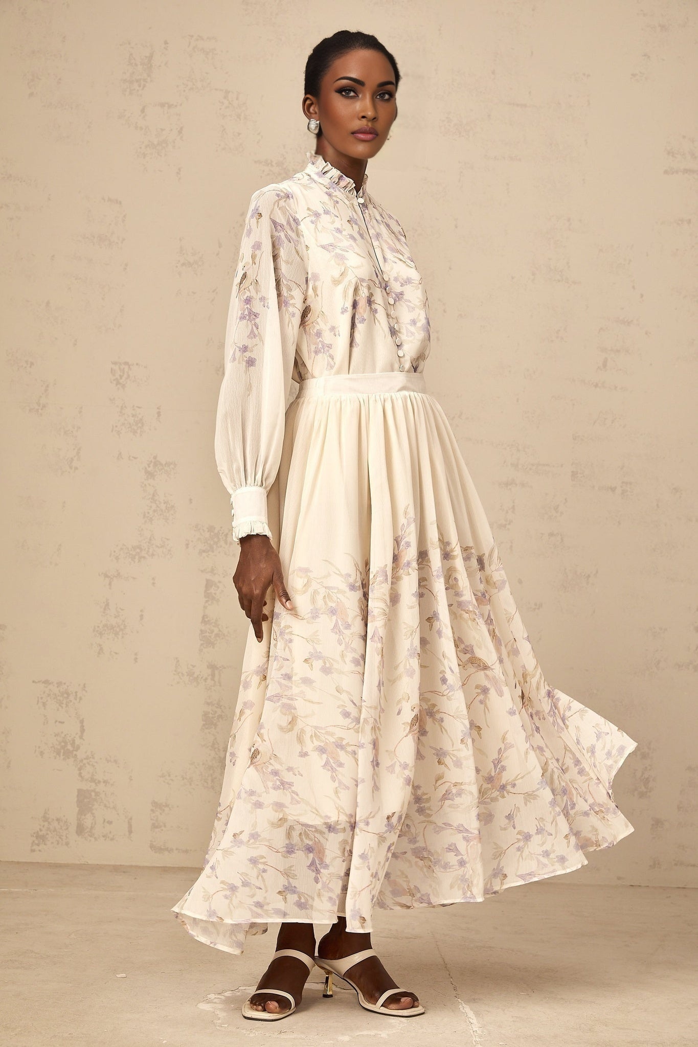 Woman wearing matching floral print shirt and skirt set Shirt has frilled details Skirt is midi length Set features wisteria pattern in blue and white tones