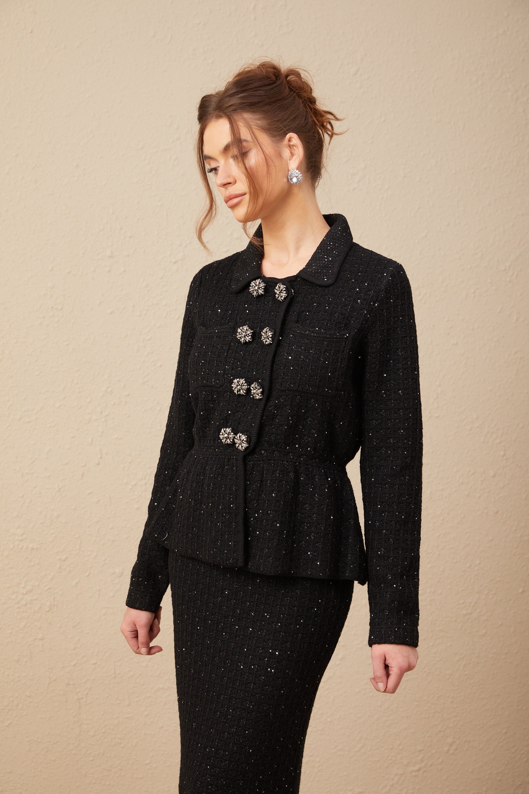 Woman wearing matching sequined waffle knit jacket and skirt set in dark color with sparkly texture