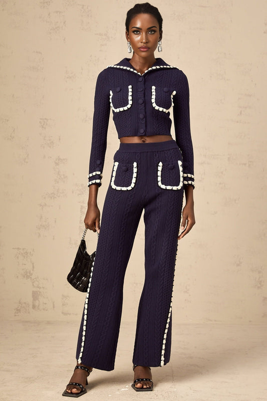 Woman wearing navy blue crochet knit cardigan and matching trousers standing against plain background