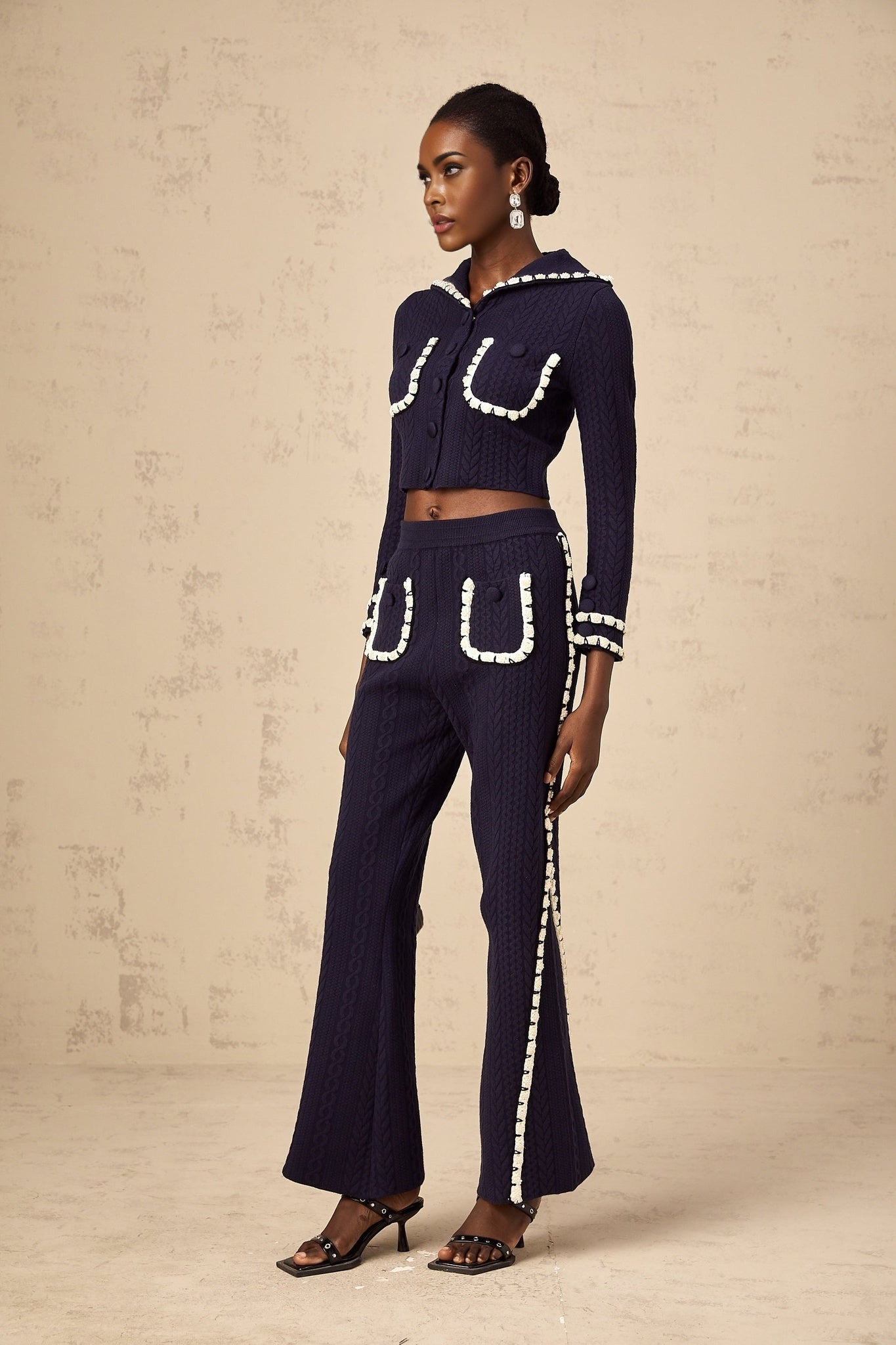 Woman wearing navy blue crochet knit cardigan and matching trousers standing in relaxed pose