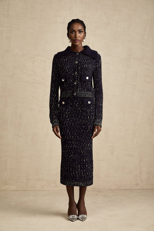 Woman wearing navy blue crochet knit jacket and matching skirt set standing against plain background