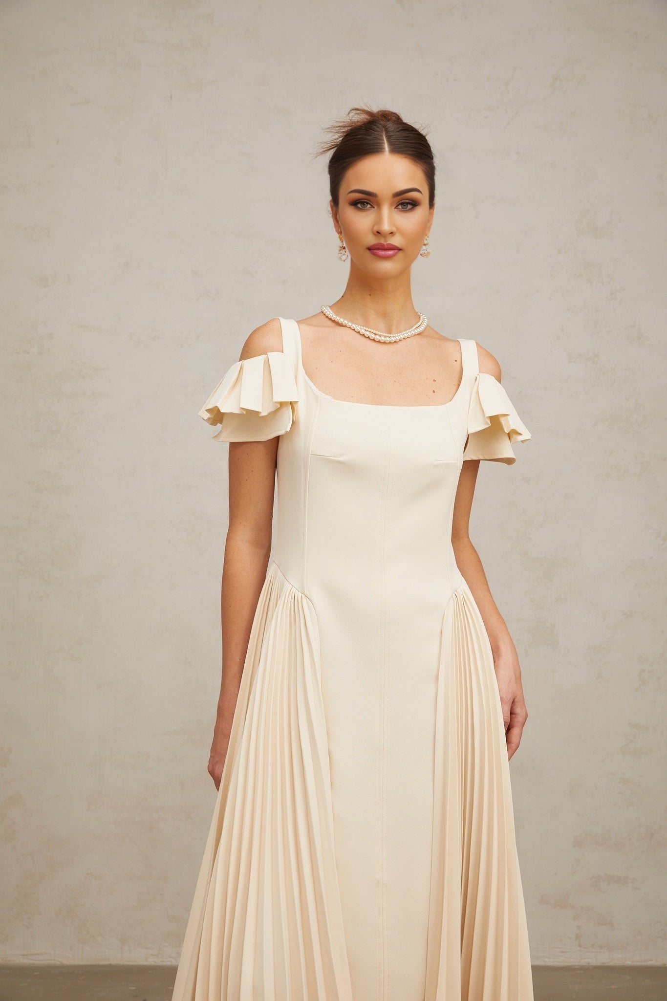 Woman wearing neutral colored pleated flared midi dress with long sleeves and v neckline