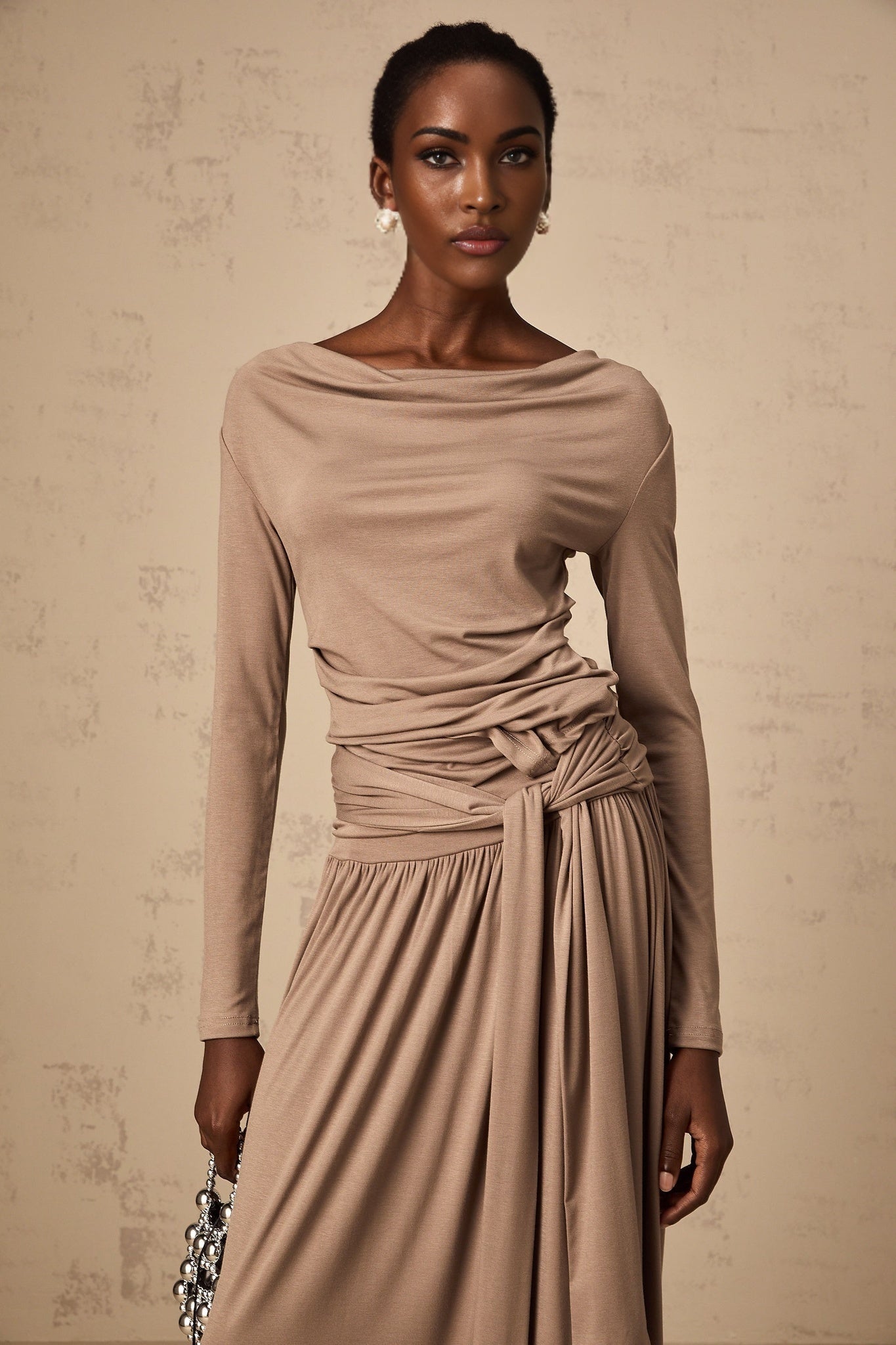 Woman wearing oatmeal colored matching set with draped top and skirt made of stretchy fabric
