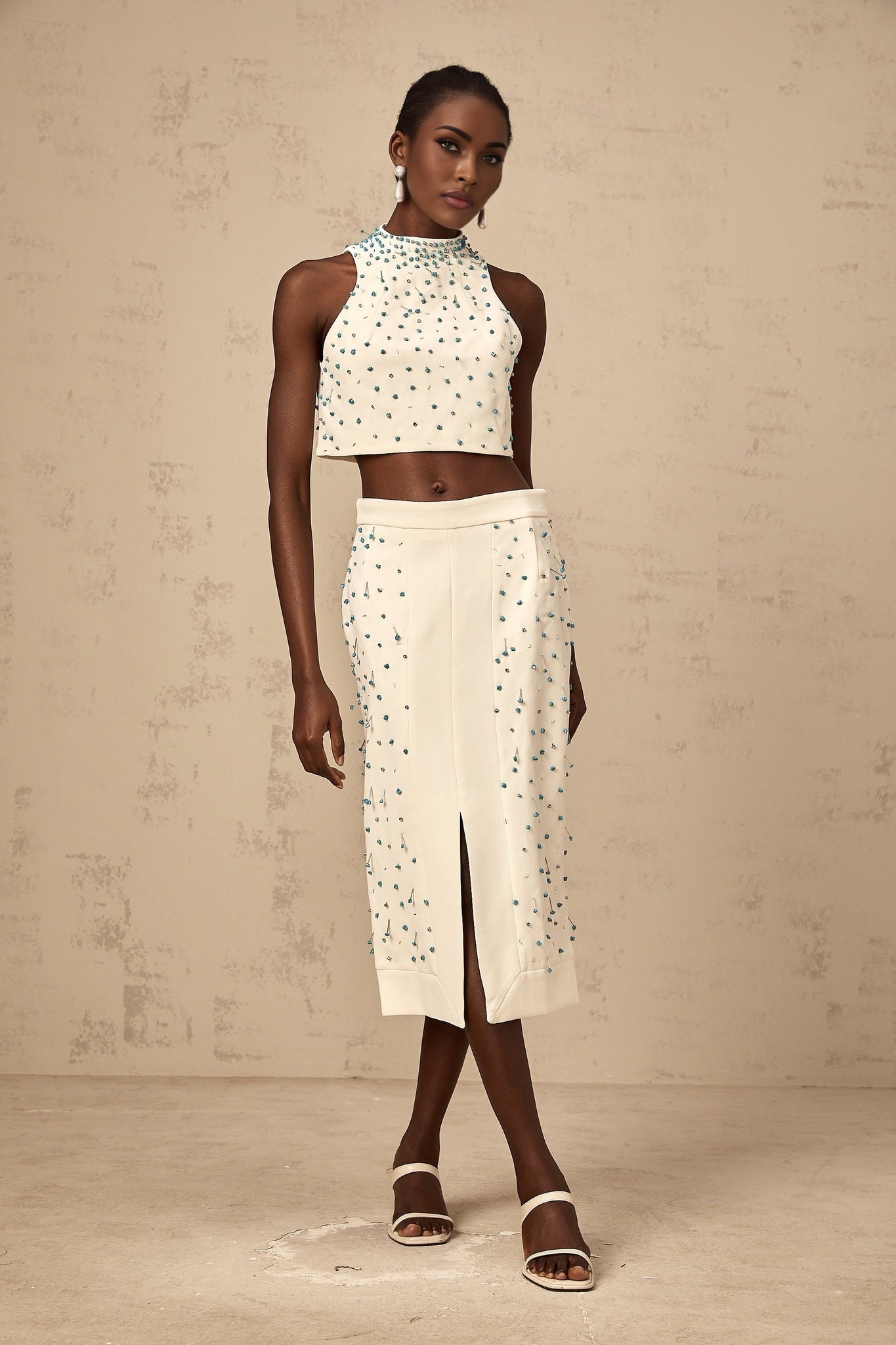 Woman wearing off white two piece outfit consisting of embellished top and matching skirt