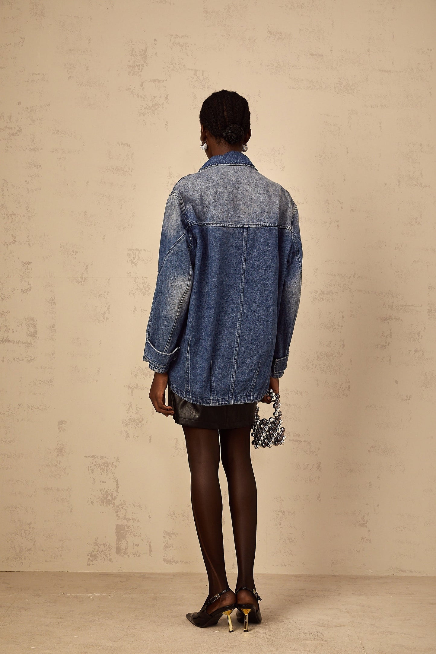 Woman wearing oversized blue denim jacket with patchwork design and loose fit