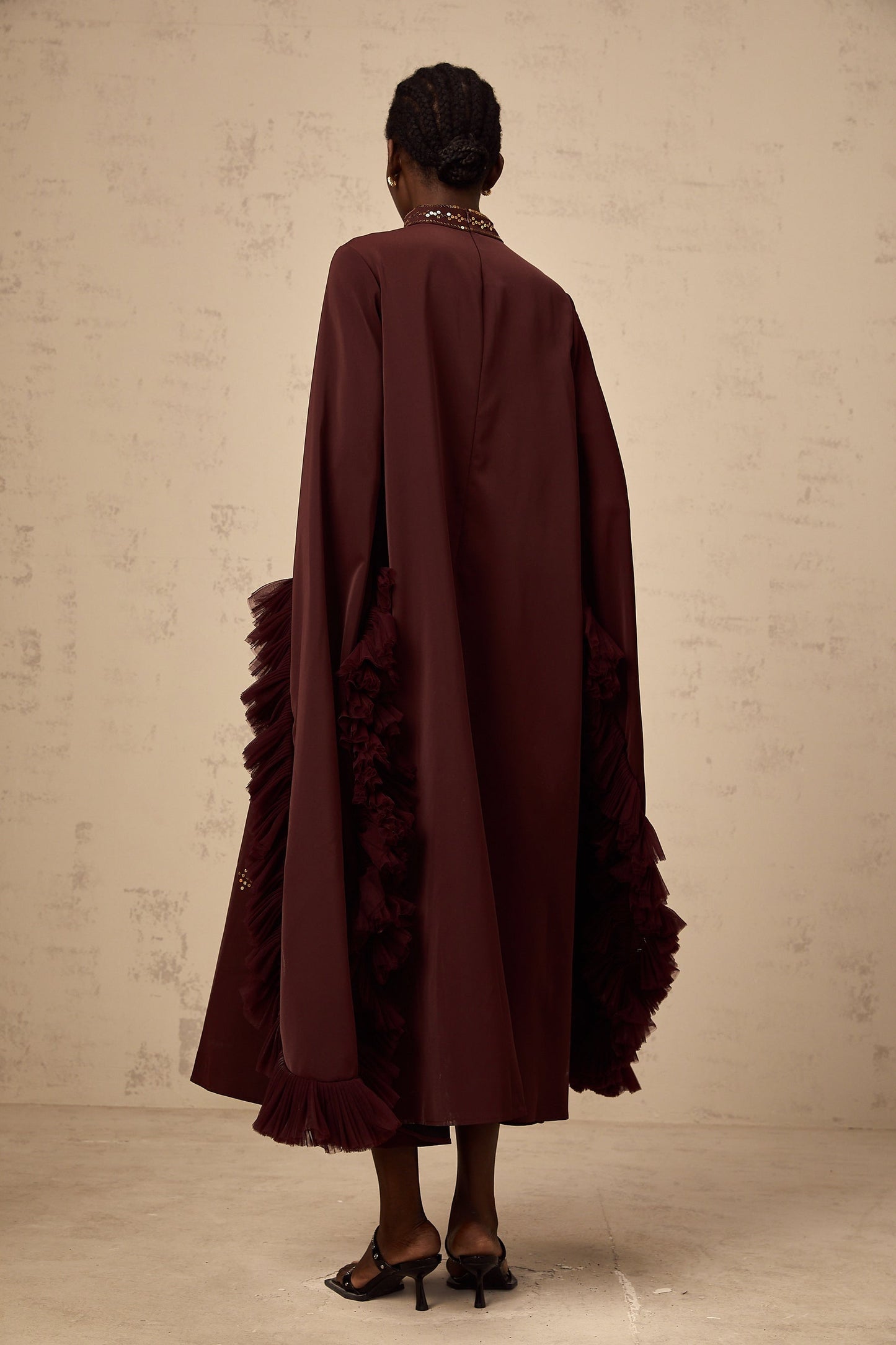 Woman wearing purple sequined midi dress with flared sleeves standing against plain background