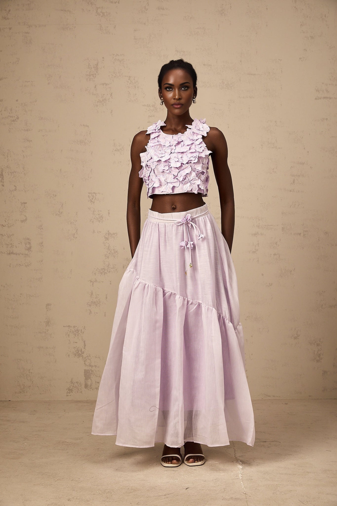 Woman wearing purple two piece outfit consisting of floral top and matching skirt with faux flower design
