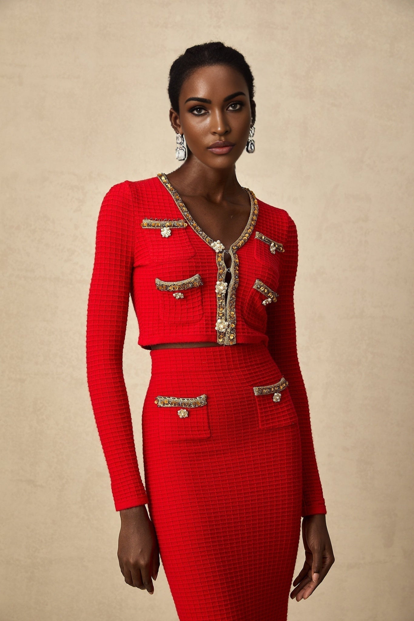 Woman wearing red knitted cardigan and matching skirt set with embellishments Cardigan has long sleeves and skirt falls below the knee Both pieces feature decorative elements