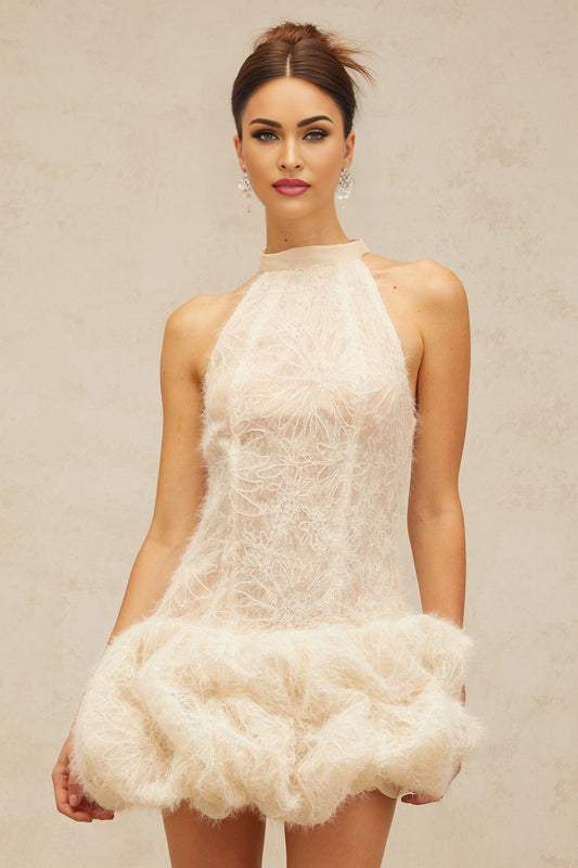 Woman wearing short beige textured mini dress with puff sleeves and round neckline standing against plain background