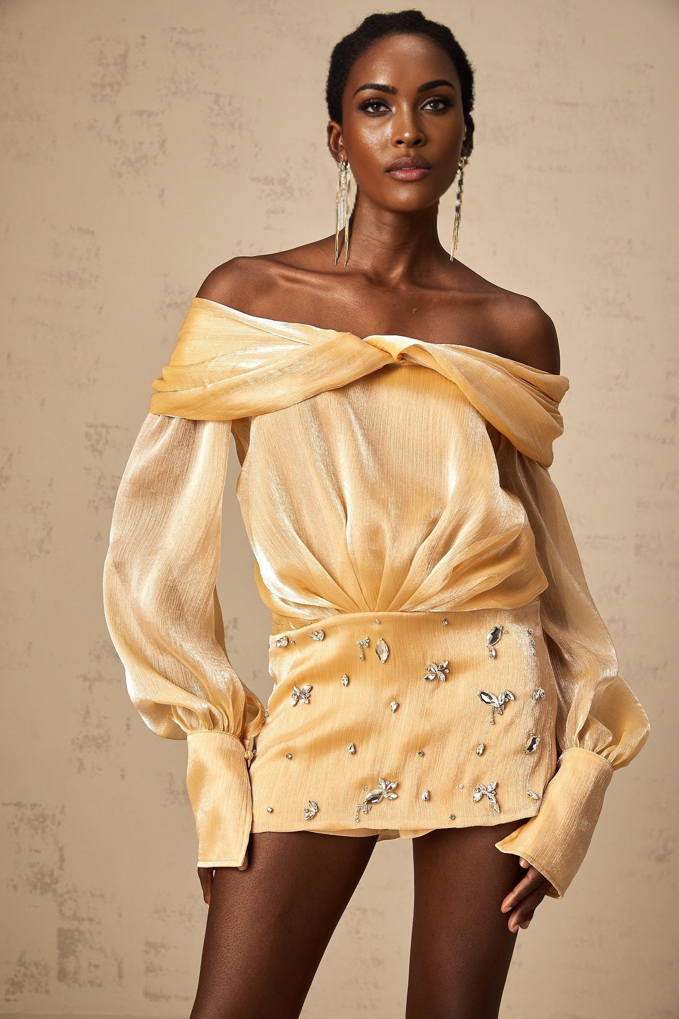 Woman wearing short gold dress with crystal embellishments and paneled design