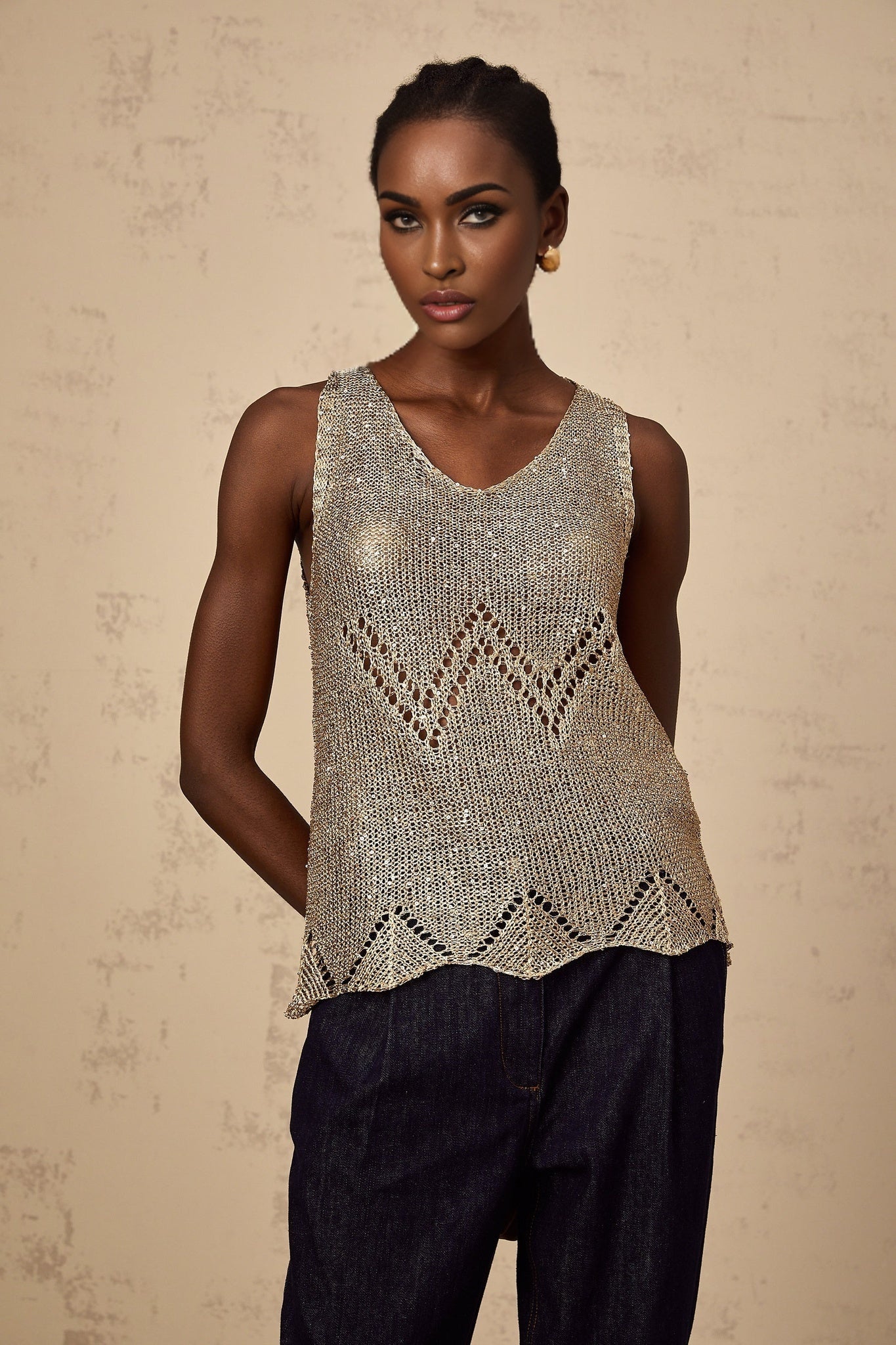 Woman wearing sleeveless gold sequined vest top with crochet pattern shimmering in light