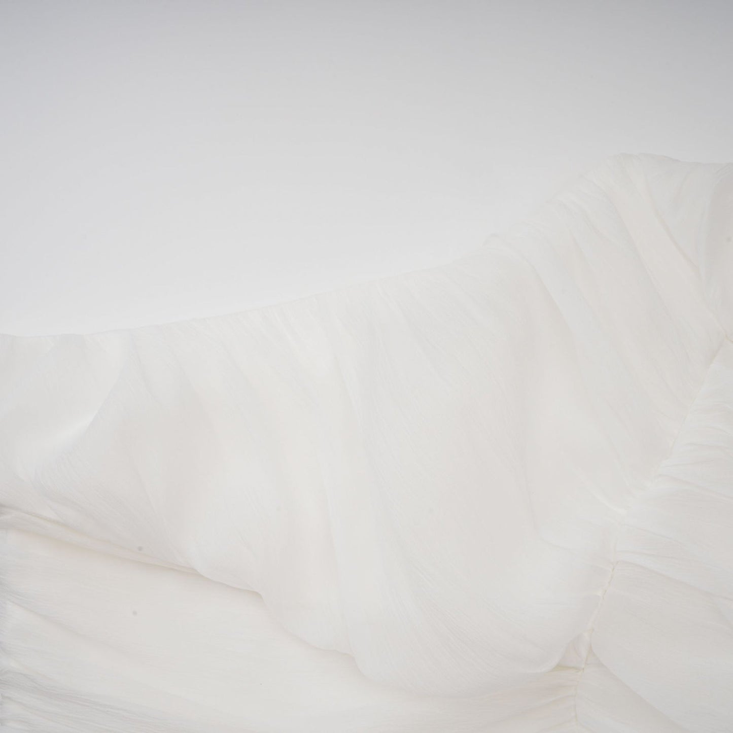 Woman wearing white creased fabric top and matching trousers standing against plain background