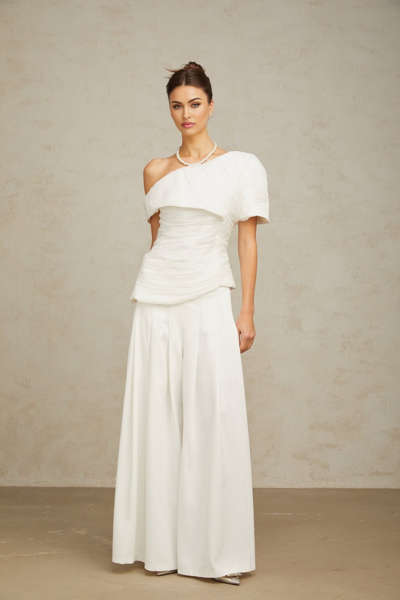 Woman wearing white creased fabric top and matching trousers standing in relaxed pose