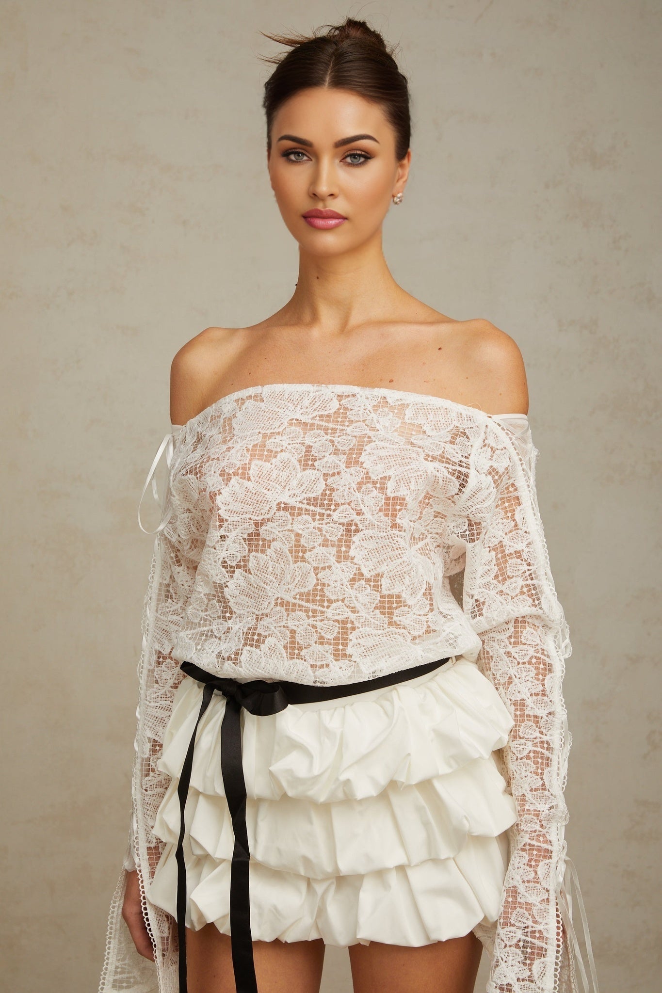 Woman wearing white floral lace top and matching skirt set standing against plain background