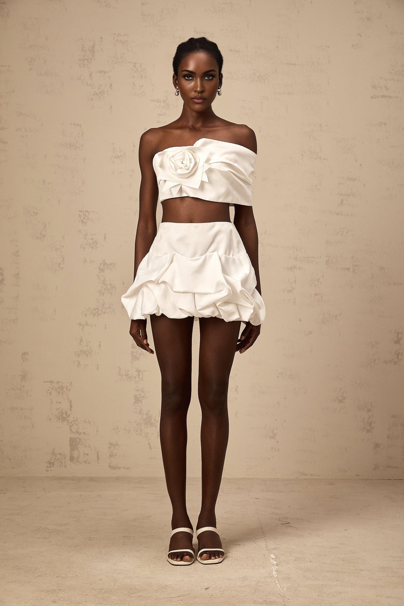Woman wearing white floral printed matching set with pleated top and skirt standing against plain background