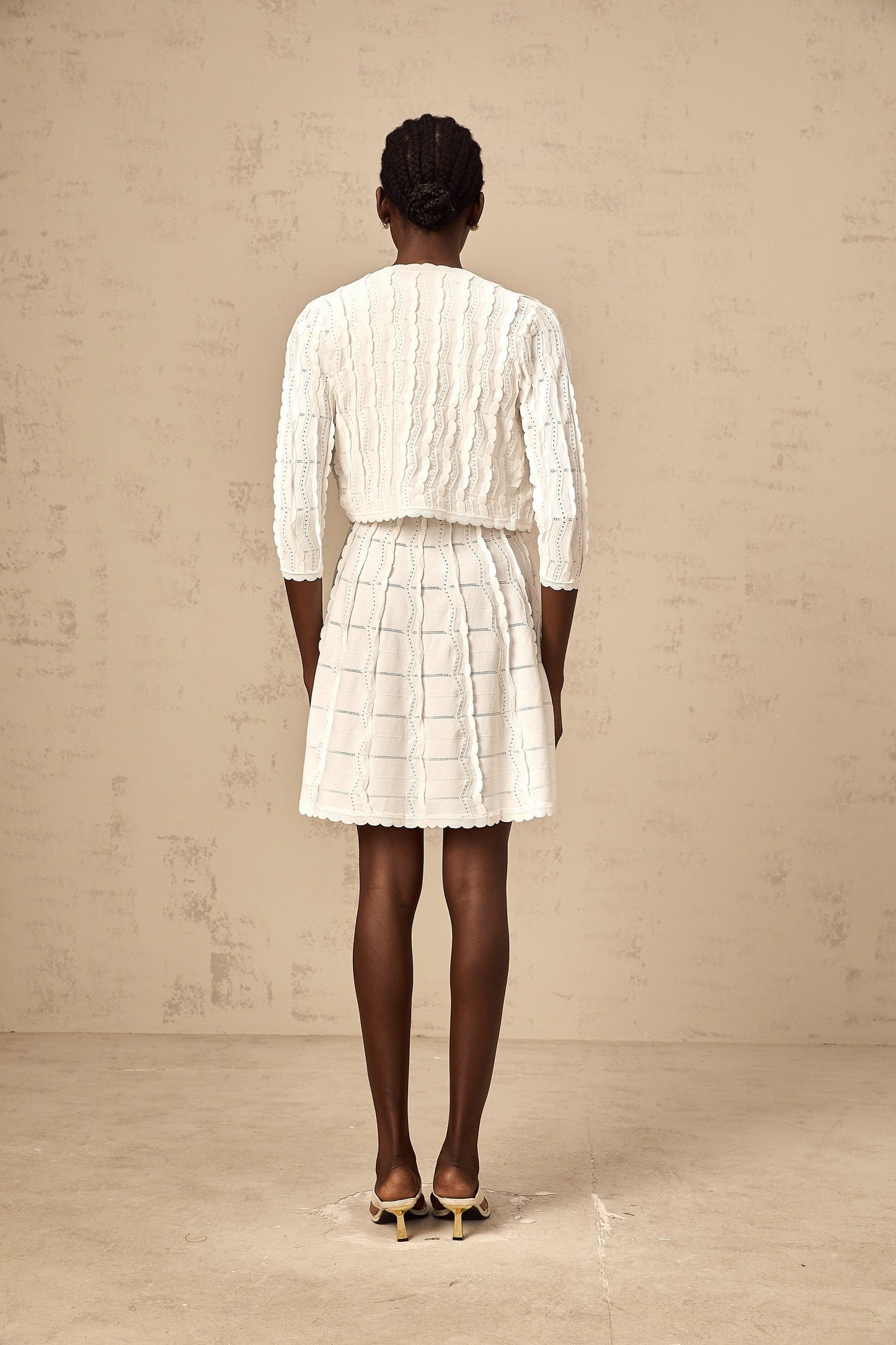 Woman wearing white knitted cardigan with ruffled details and long sleeves