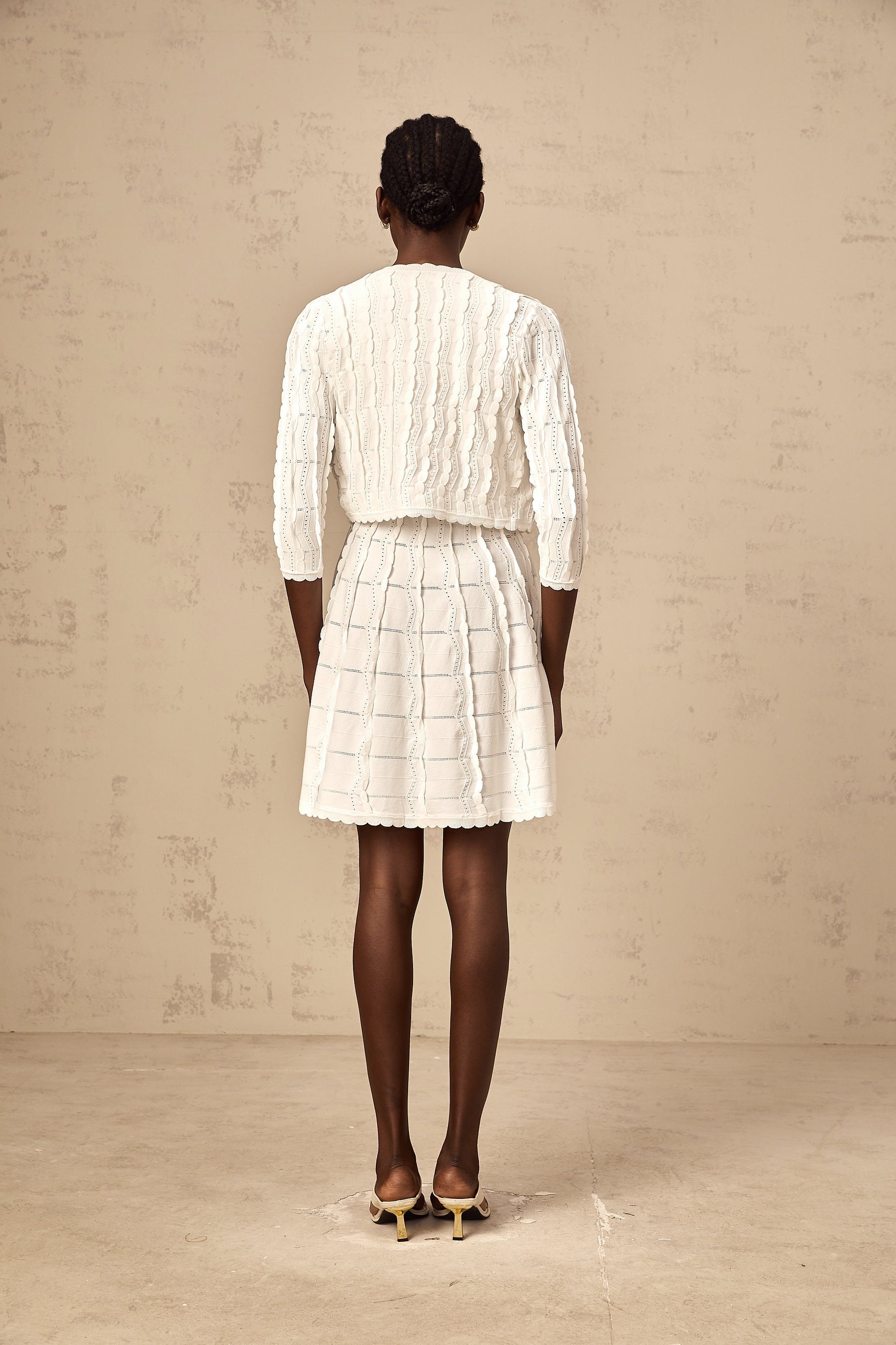 Woman wearing white knitted cardigan with ruffled details and long sleeves