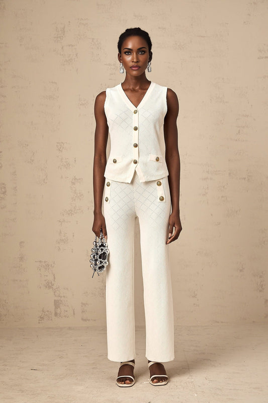 Woman wearing white knitted sleeveless top and matching trousers standing against plain background